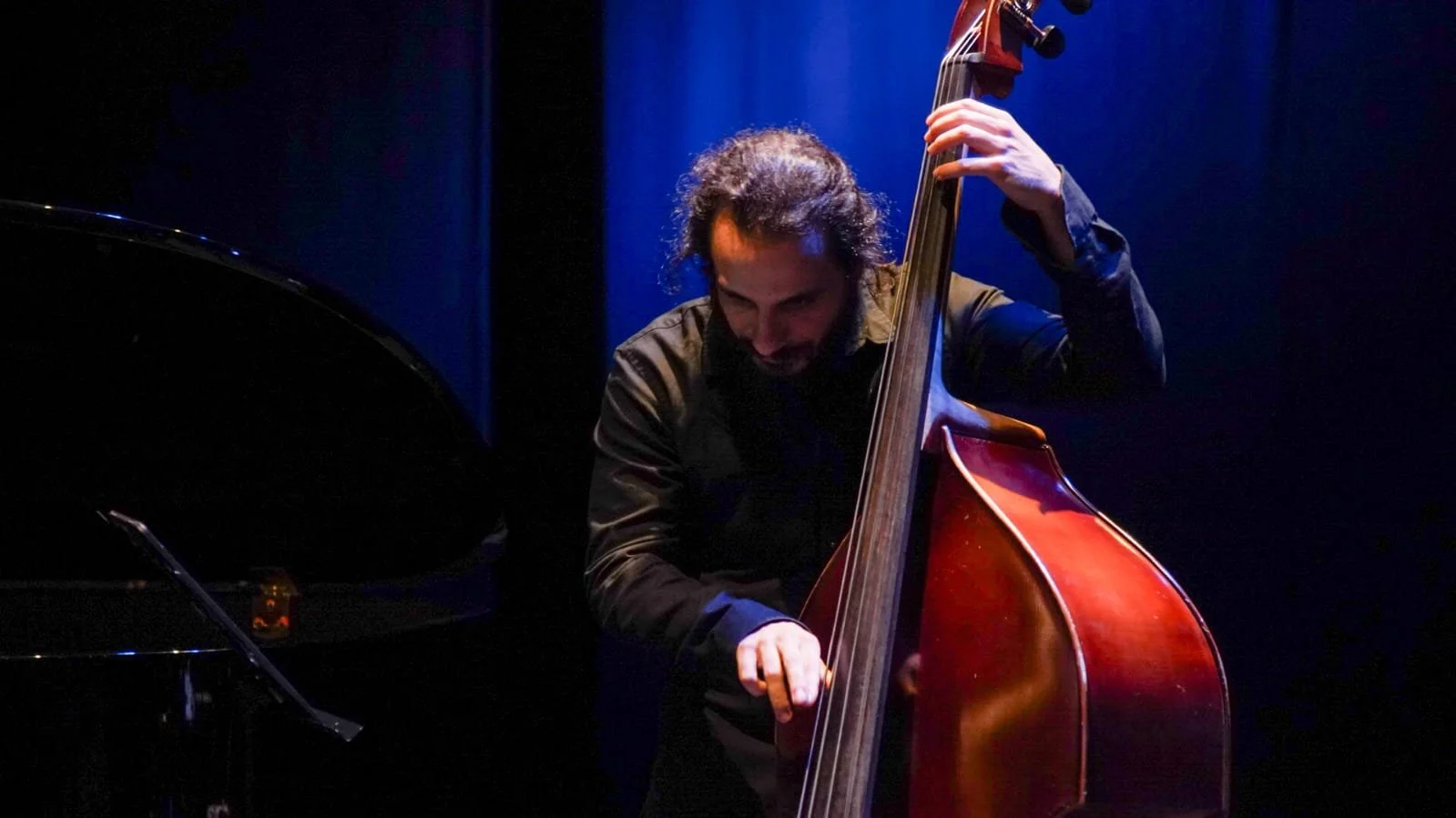 Musician playing double bass on stage with dark background.