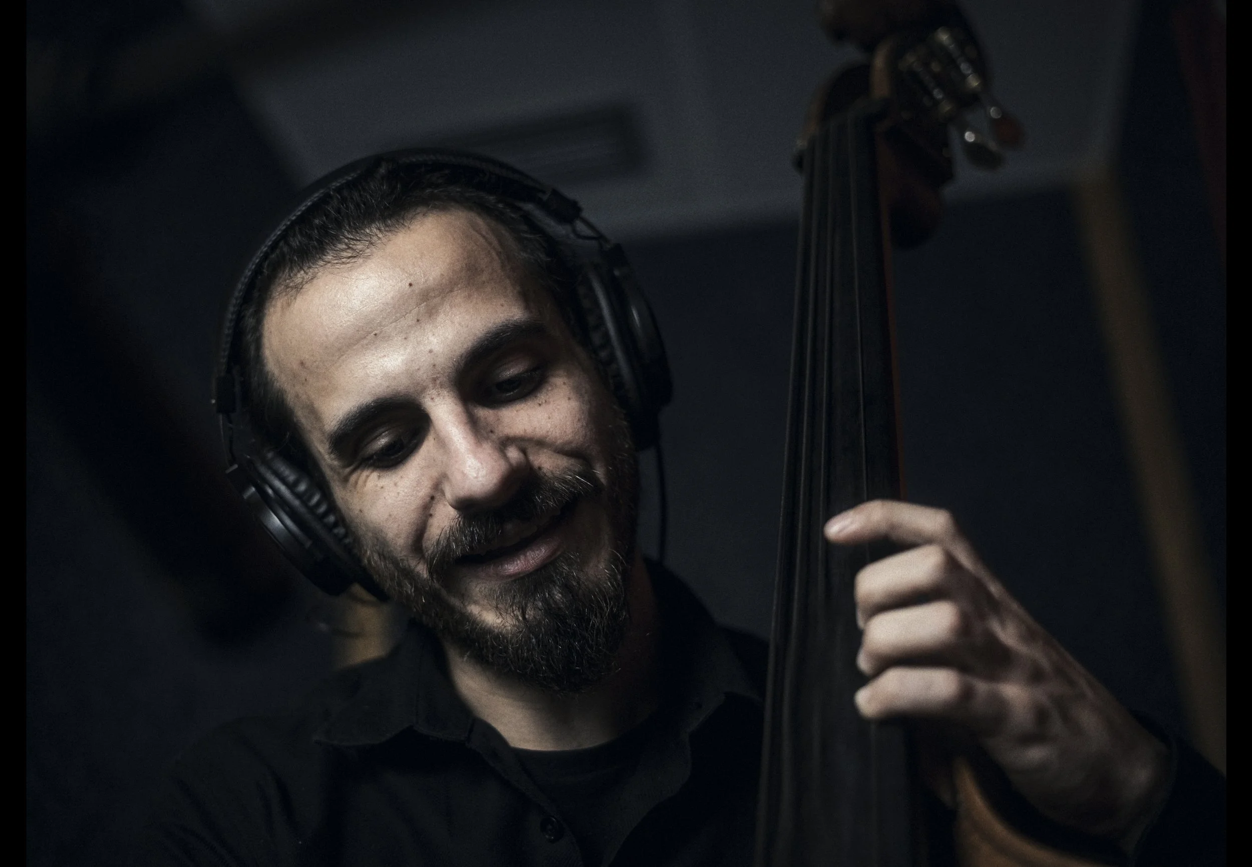 A man wearing headphones playing a double bass.