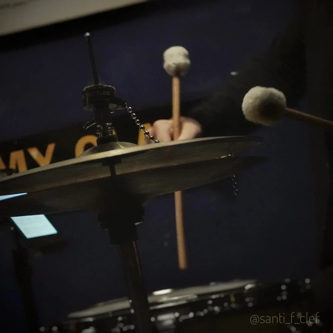 Close-up of a drum set with drumsticks resting on the drum, a cymbal in the foreground, and a dark background.
