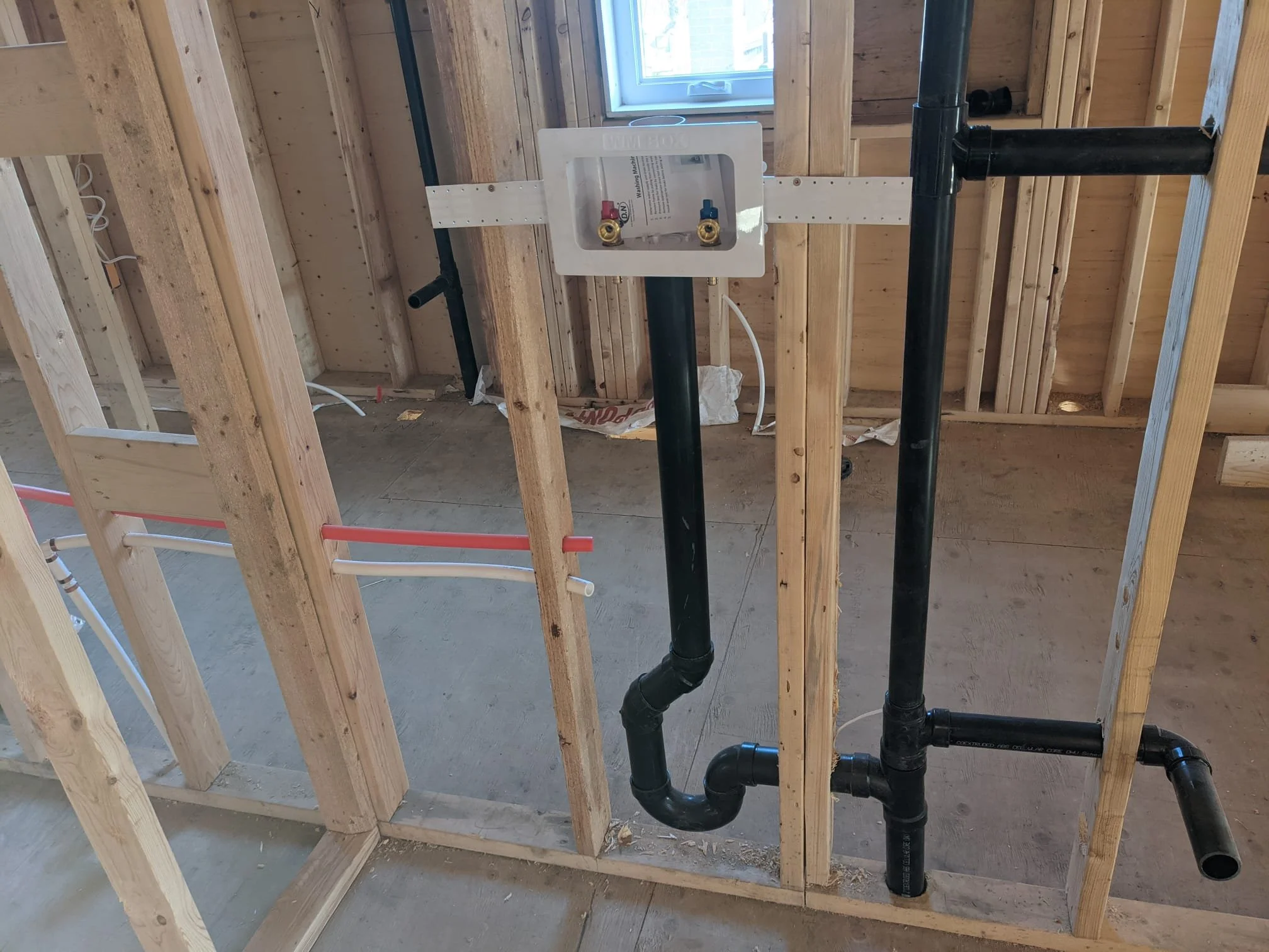 Plumbing pipes and a water shut-off valve in a house under construction, with exposed wooden framing and a window in the background.