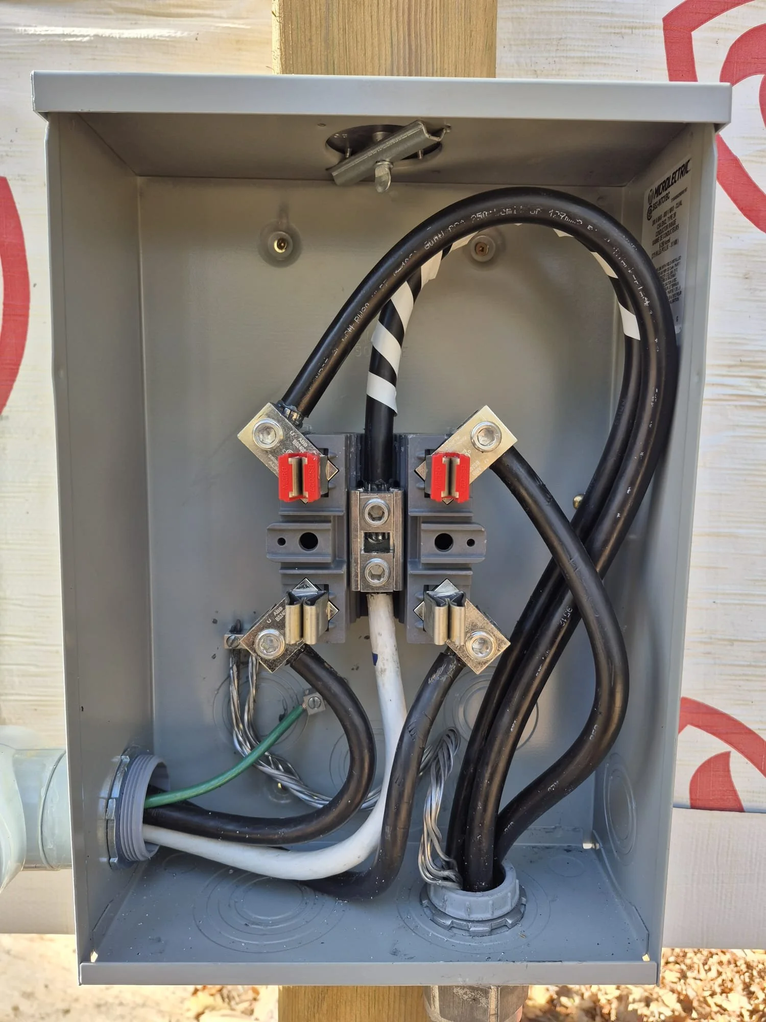 Electrical meter box with black, white, and green wires connected to electrical terminals inside a gray metal enclosure.