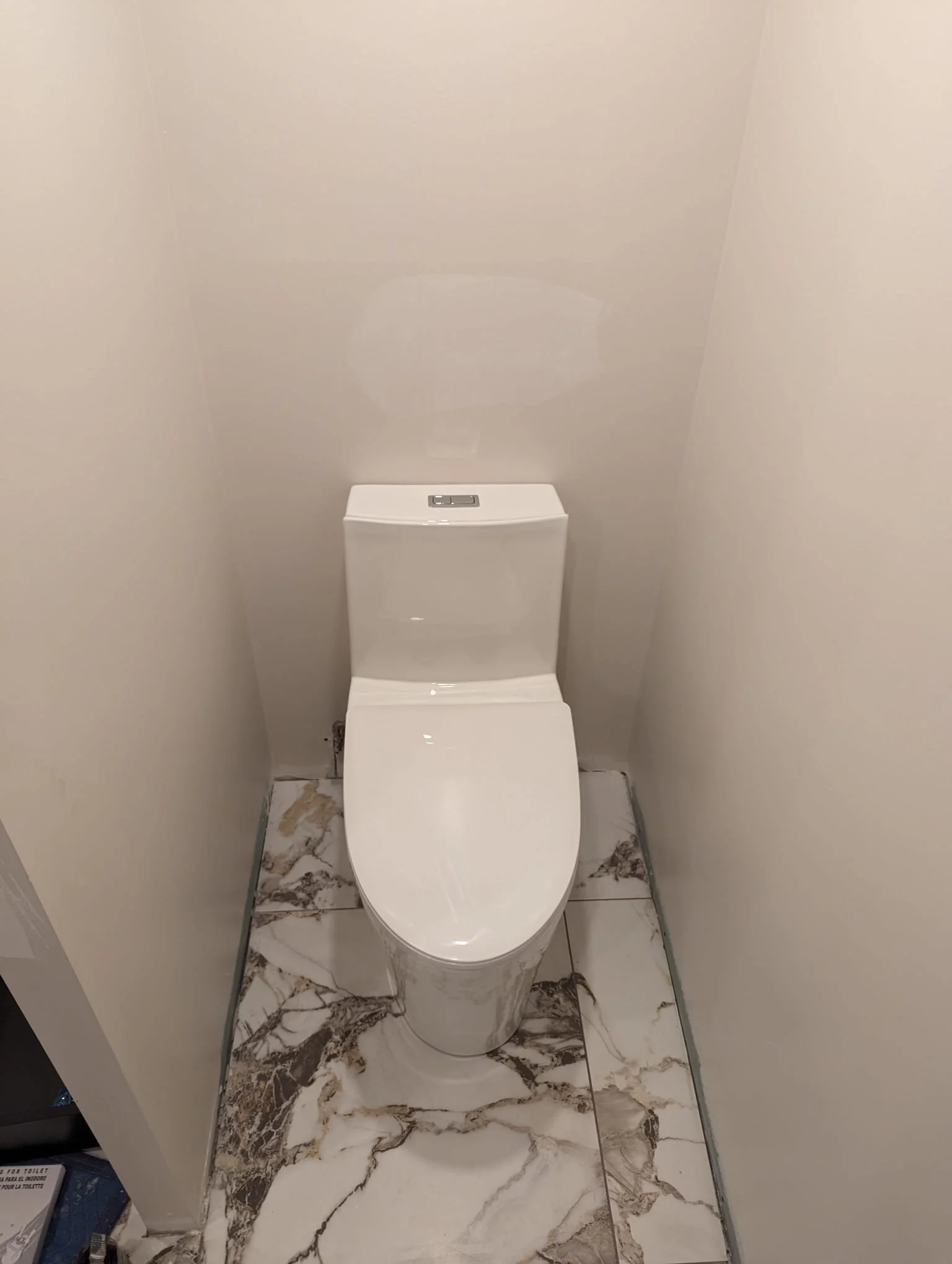 Modern white toilet in a small, clean bathroom with marble floor tiles.