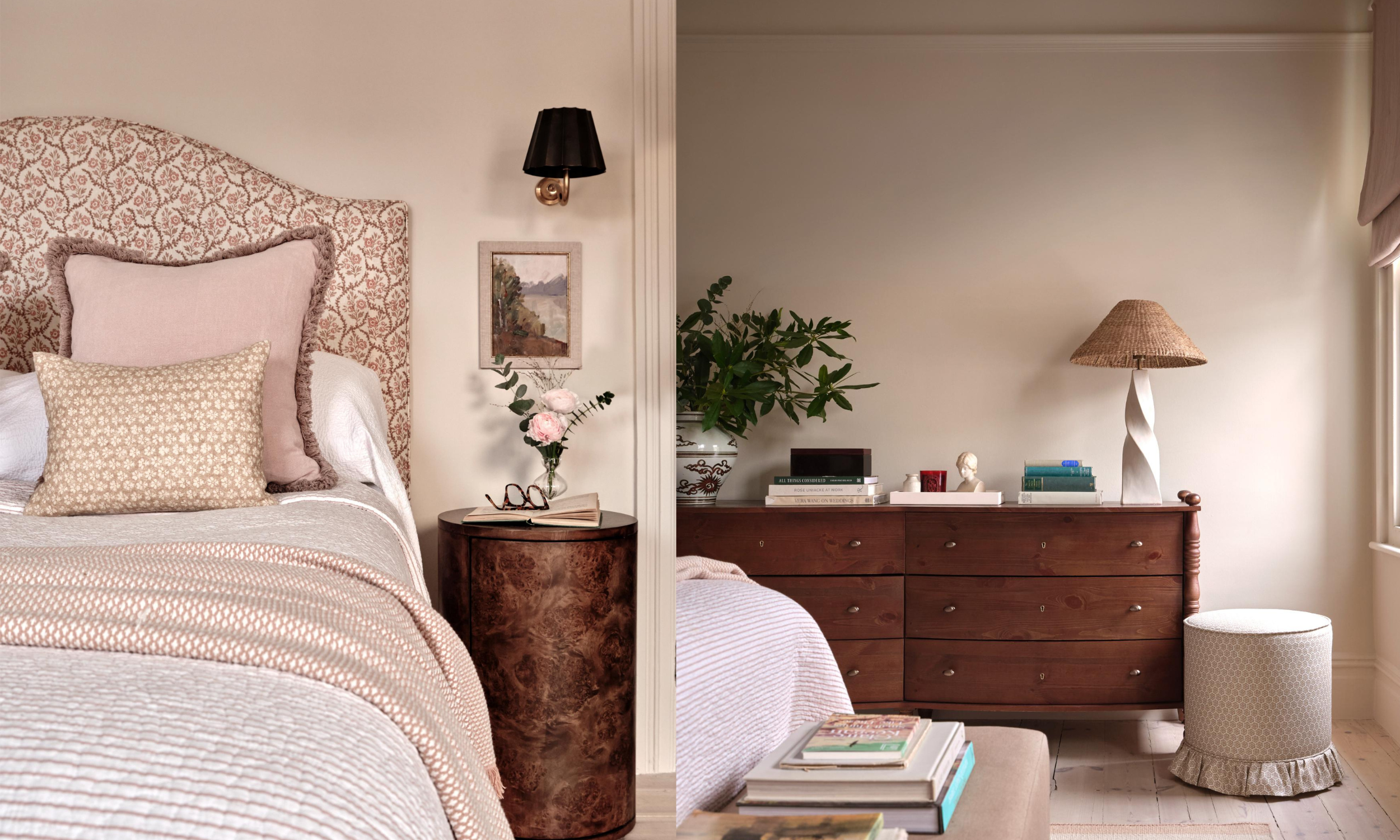 A bedroom divided in half with a bed on the left and a wooden dresser on the right. The left side has an ornate beige and pink headboard, pink and patterned pillows, a bedside table with a flower vase, and a black wall sconce. The right side features