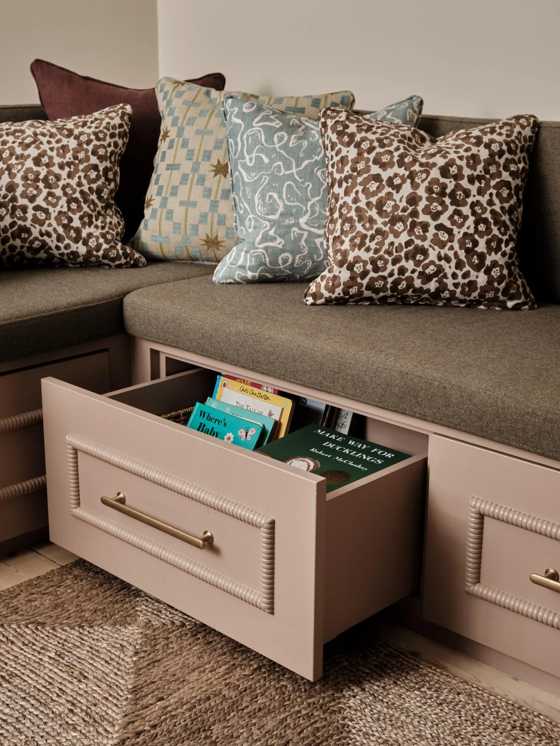 A sofa with multiple decorative pillows and a coffee table drawer filled with children's books.