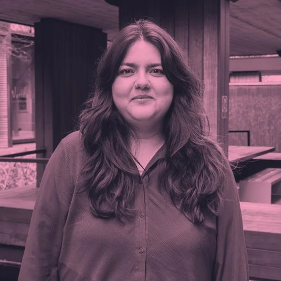 A woman with long wavy hair standing outside on a wooden patio area.