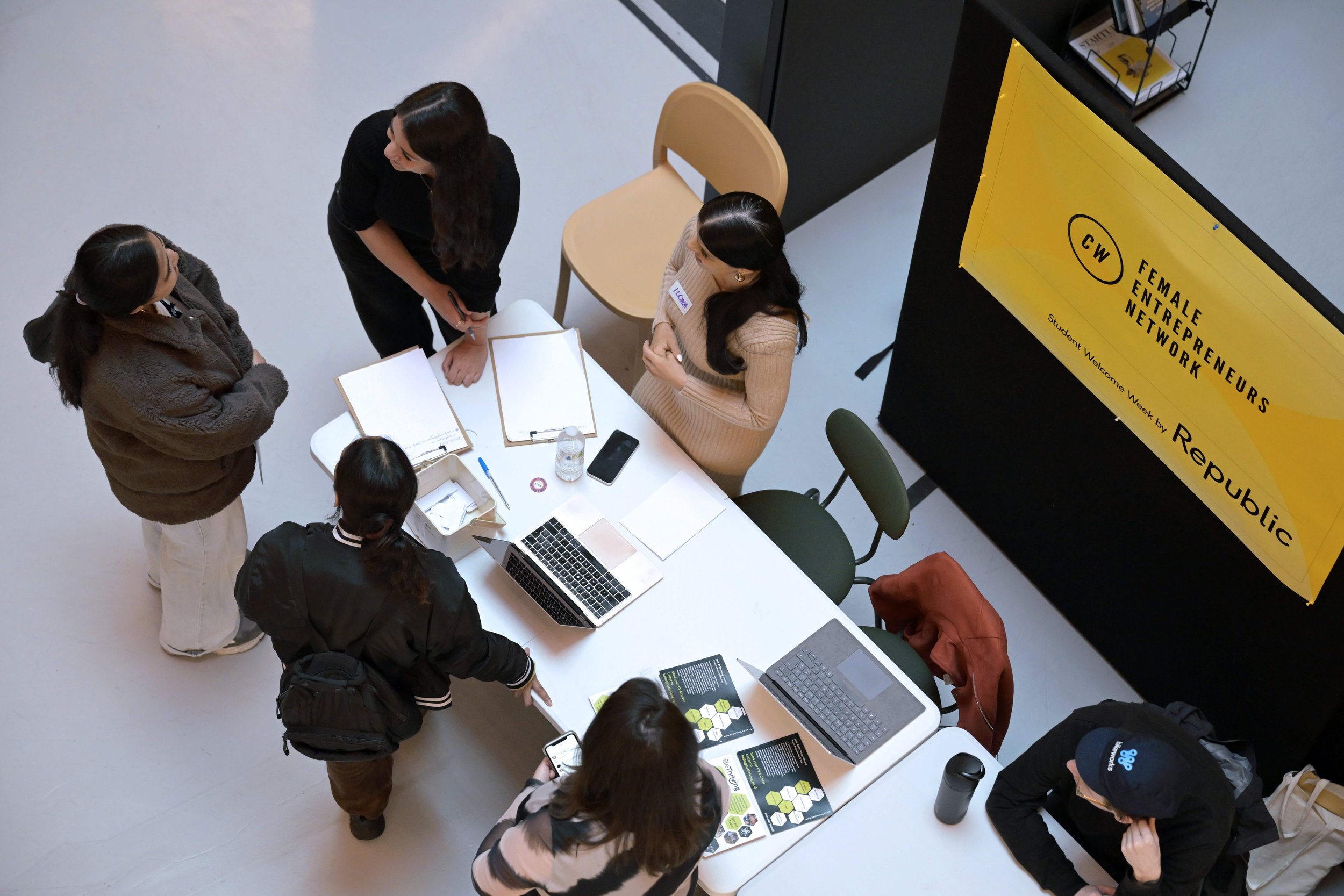 People gathered around a table at an event with a yellow banner reading 'Female Entrepreneurs Network' and 'Student Welcome Week by Republic'.