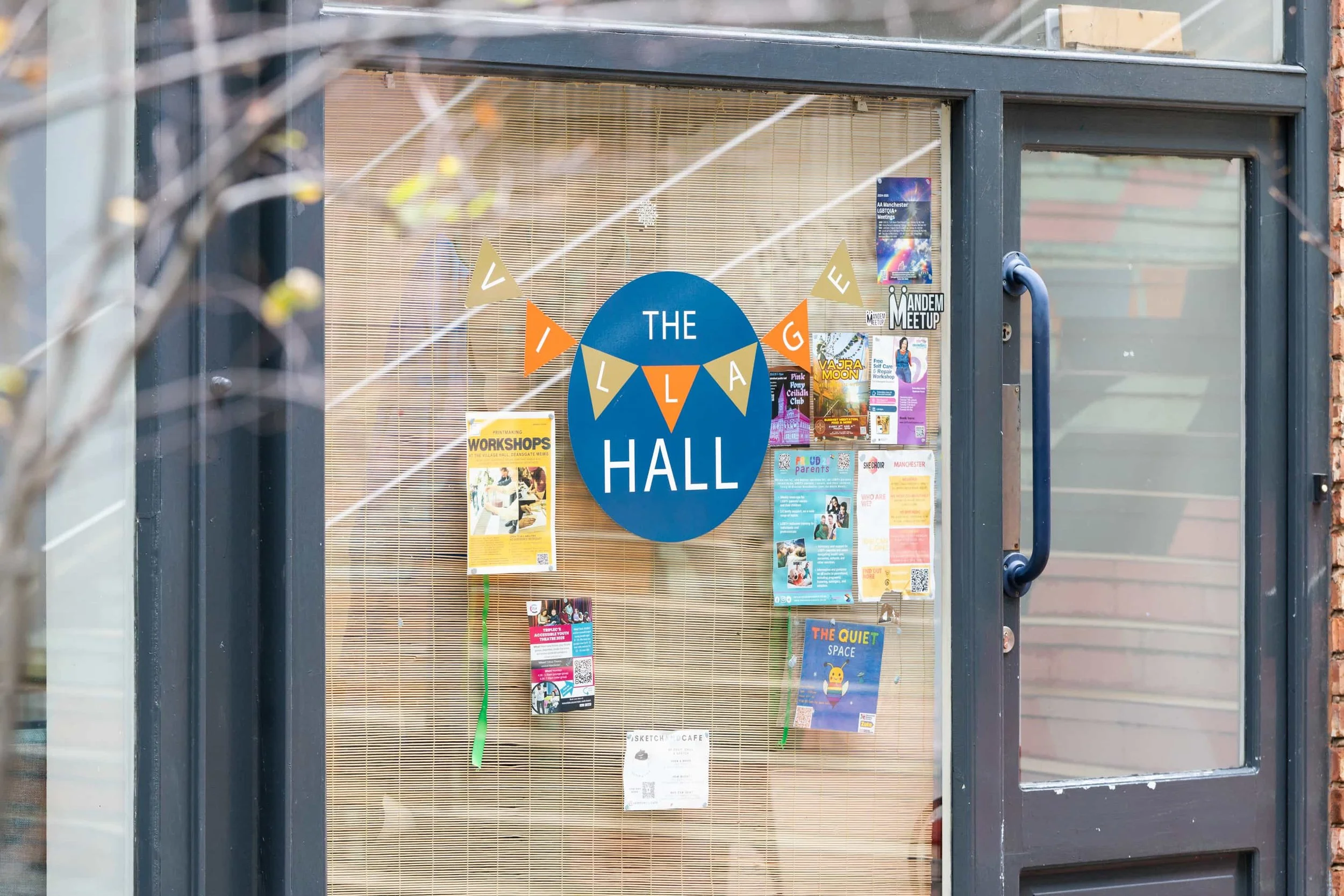 Glass door with various flyers and posters, and a circular sign that says "The Village Hall" with triangular banners spelling "VILLAGE" above it.