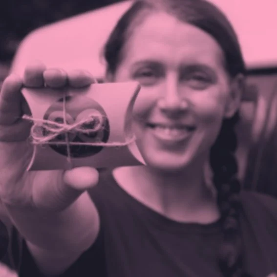 Smiling woman with braided hair taking a photo with a smartphone, holding it close to the camera, outdoors with a pink tint overlay.
