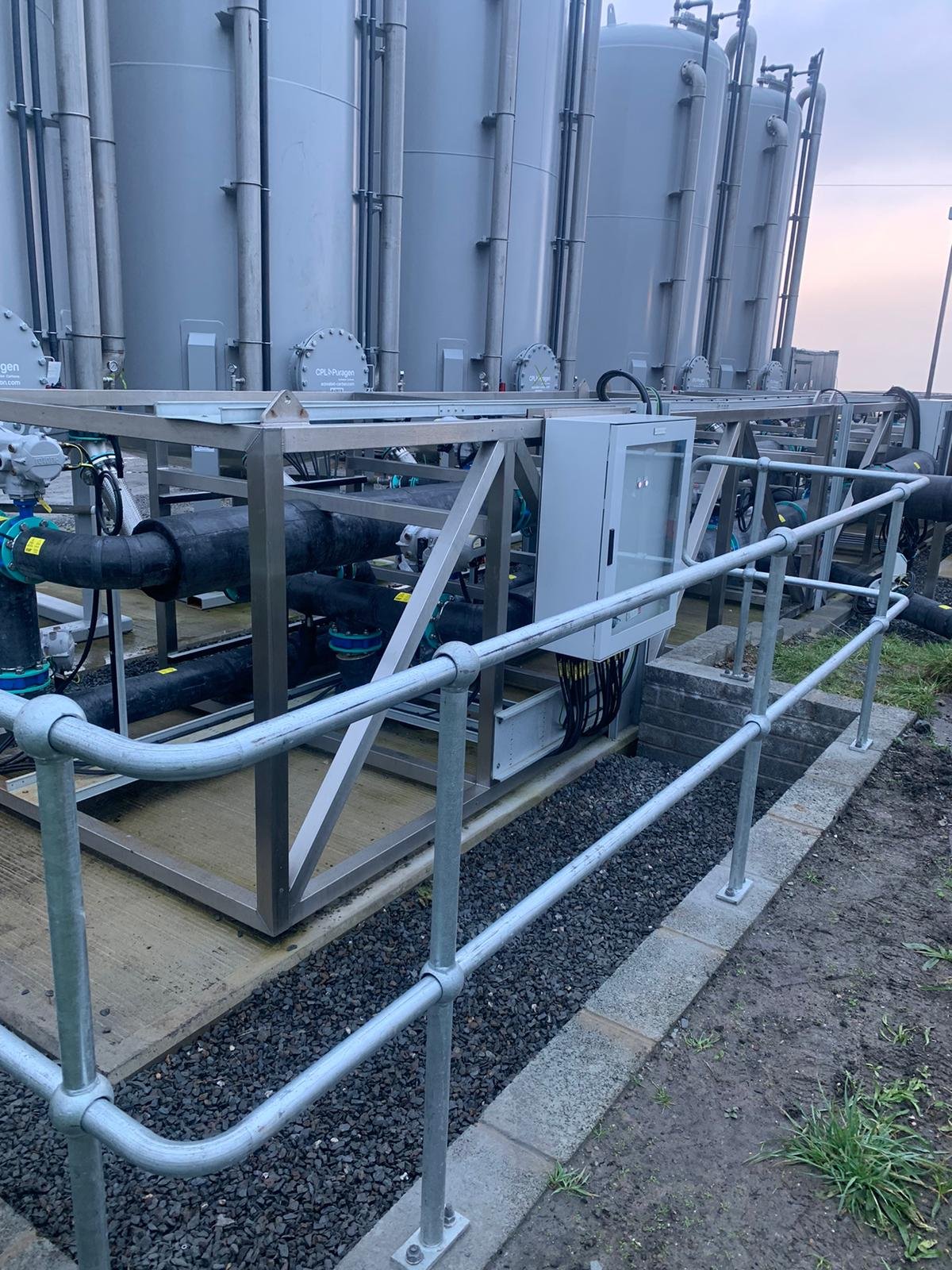 Industrial equipment with pipes and control box outside on a concrete platform, surrounded by a metal safety railing.