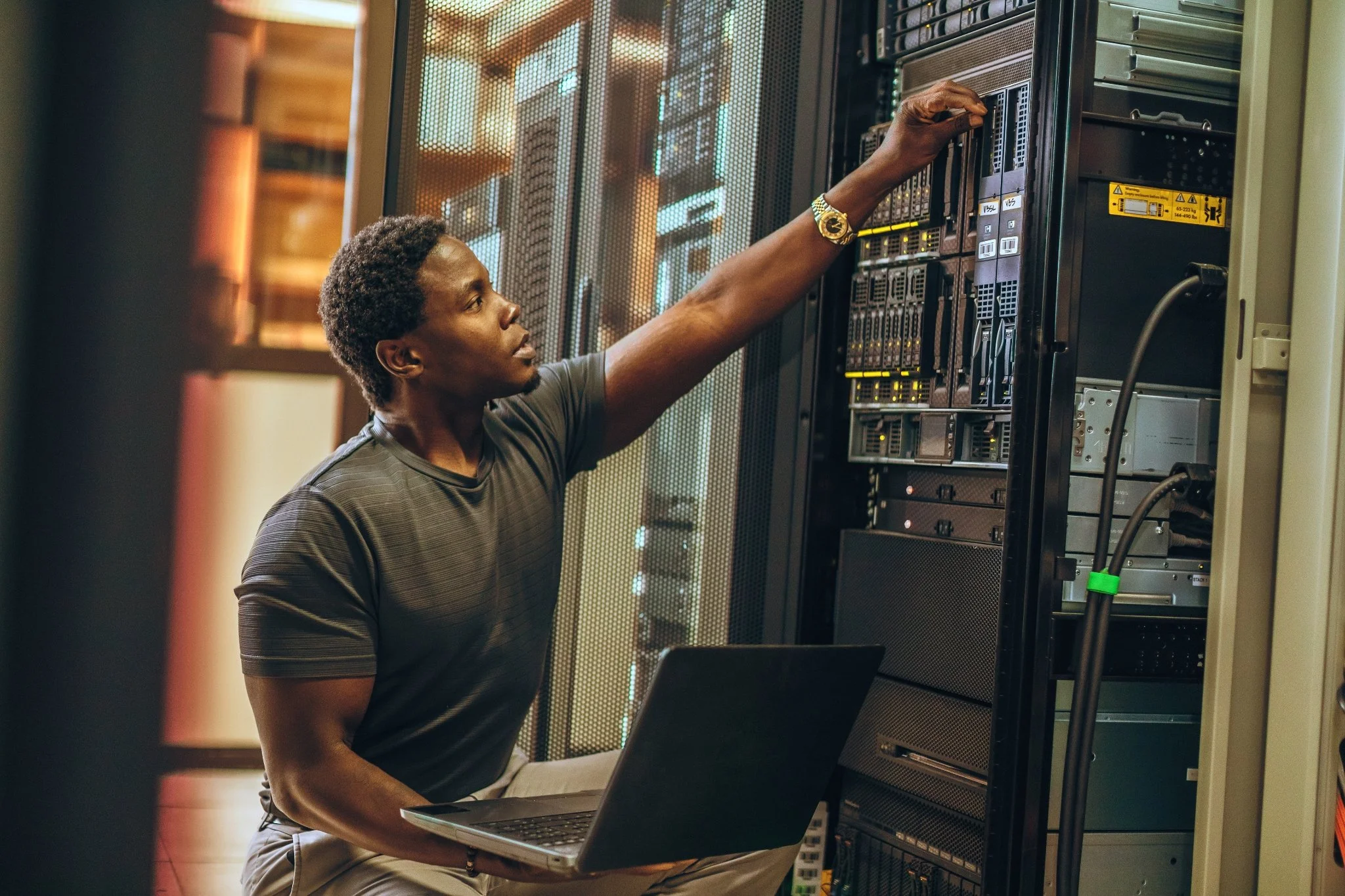 A man working on a server in a data center, holding a laptop and adjusting equipment.