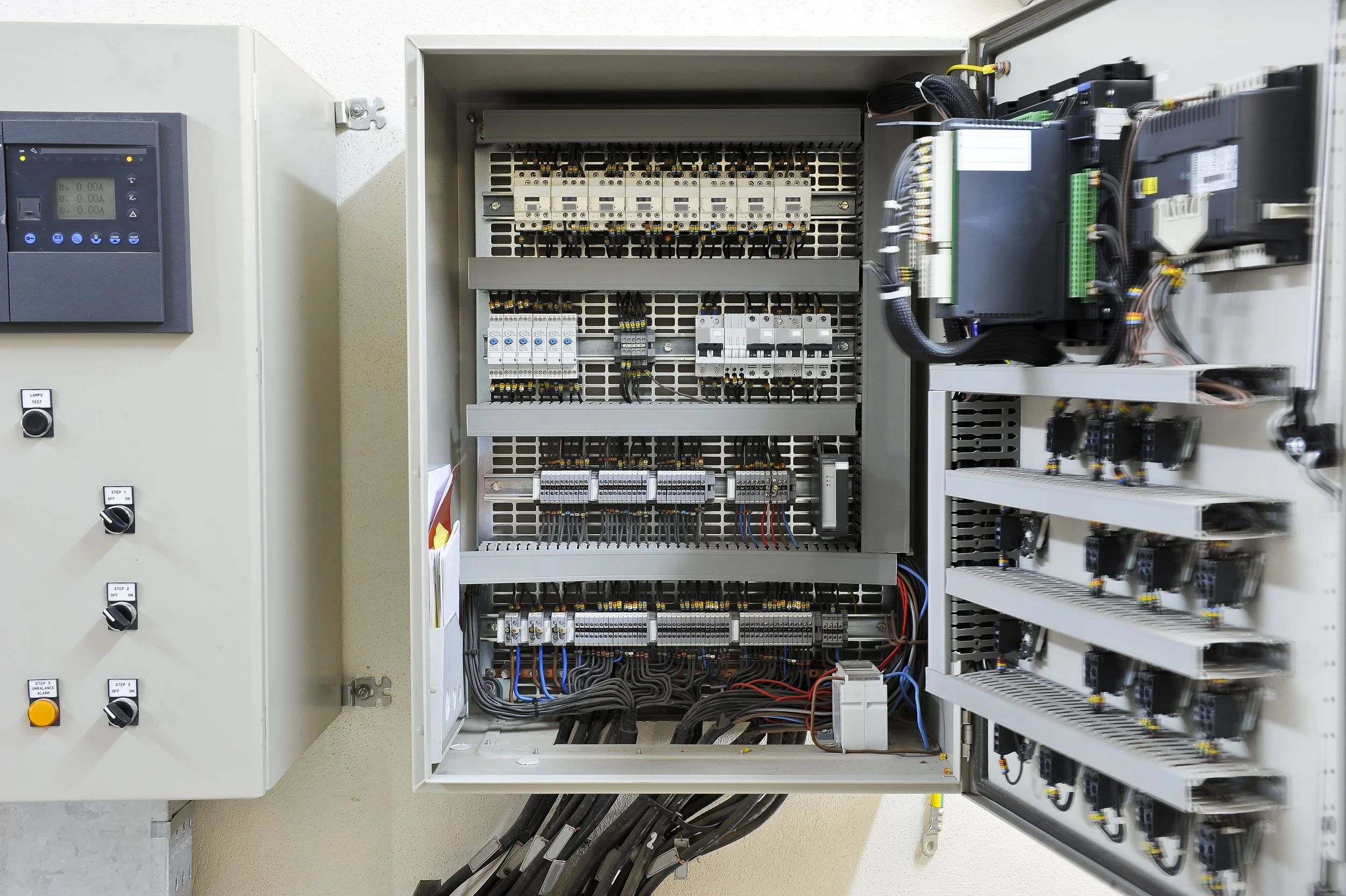 An open electrical control panel with various relays, circuit breakers, and wiring inside.