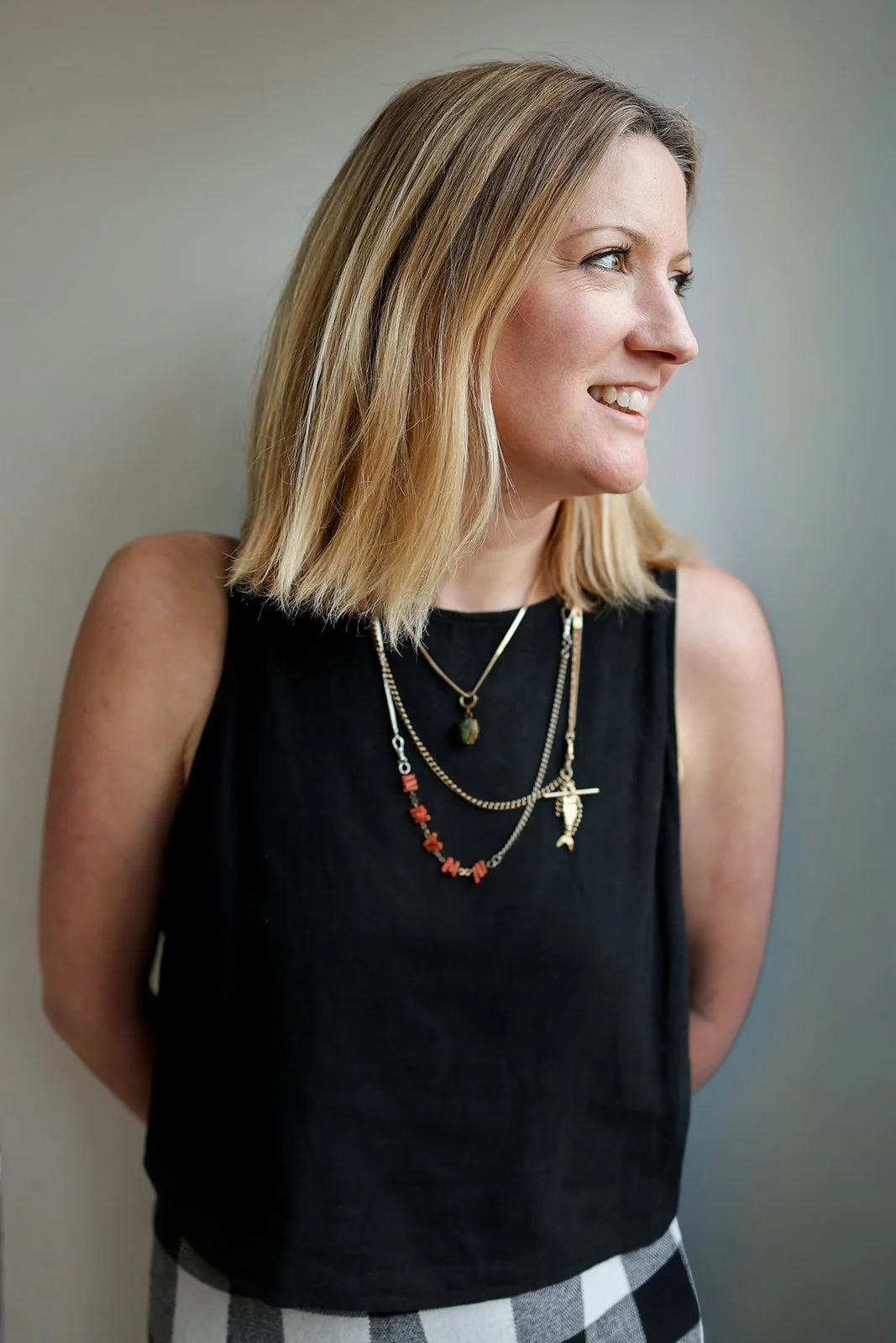 A picture of Caroline Ramsey, the founder of Jewellery brand The Windsor Archive. A woman with shoulder-length blonde hair, wearing a black sleeveless top and layered necklaces, smiling and looking to the right.