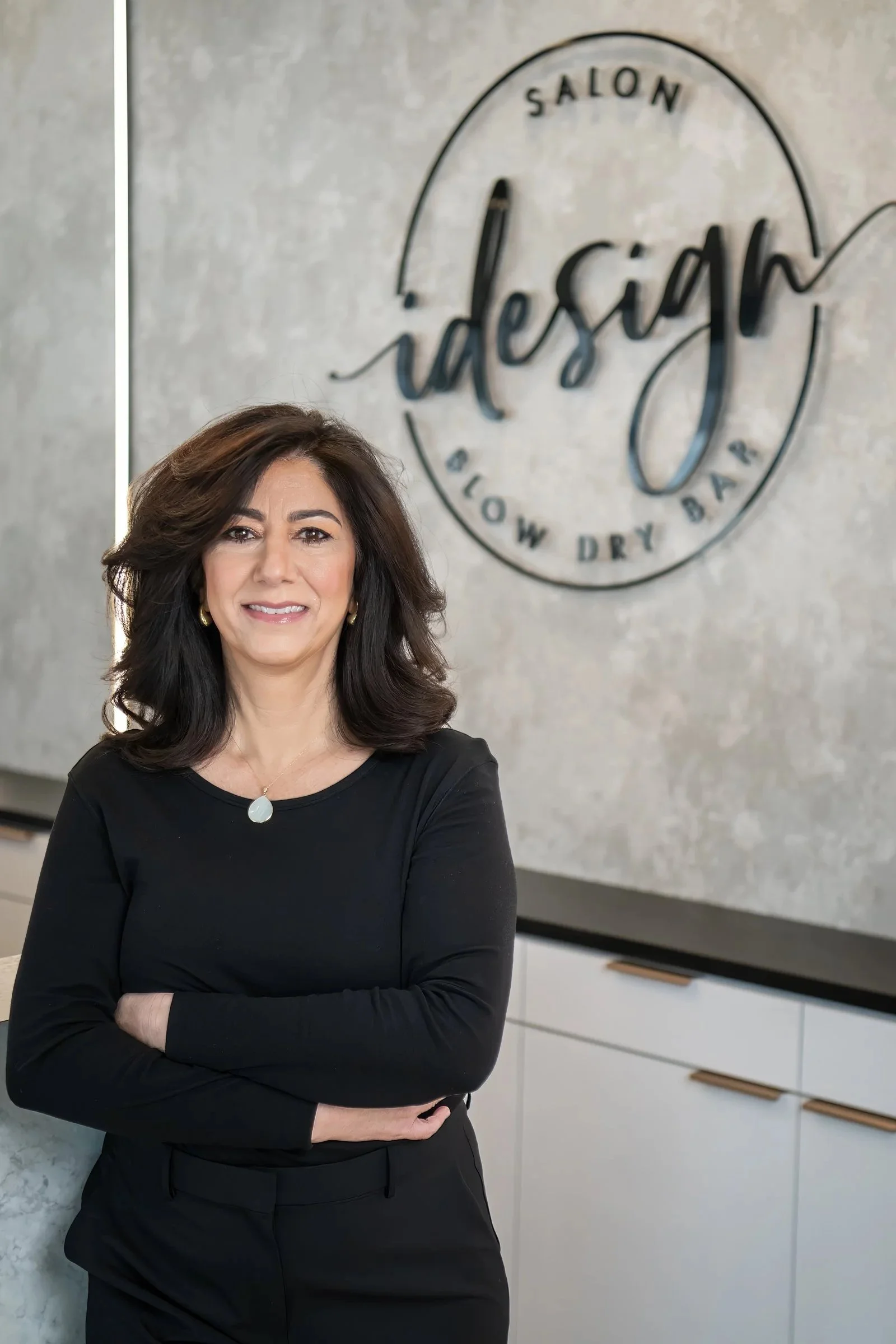 A woman standing with arms crossed in front of a sign that reads 'Salon istory Glow Dry Bar'