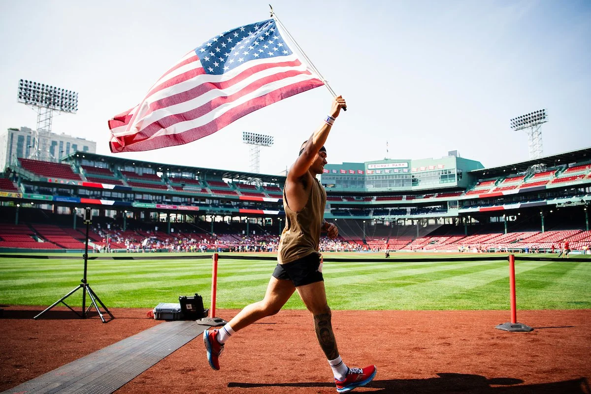 A person running on a track at a stadium, holding an American flag.