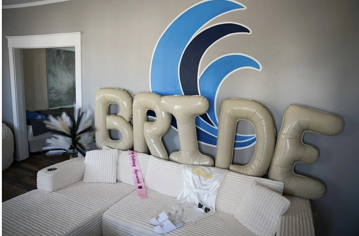 Living room with a large sofa, decorative balloons spelling out 'BRIDE,' and a wall sign featuring blue and navy ocean wave designs.
