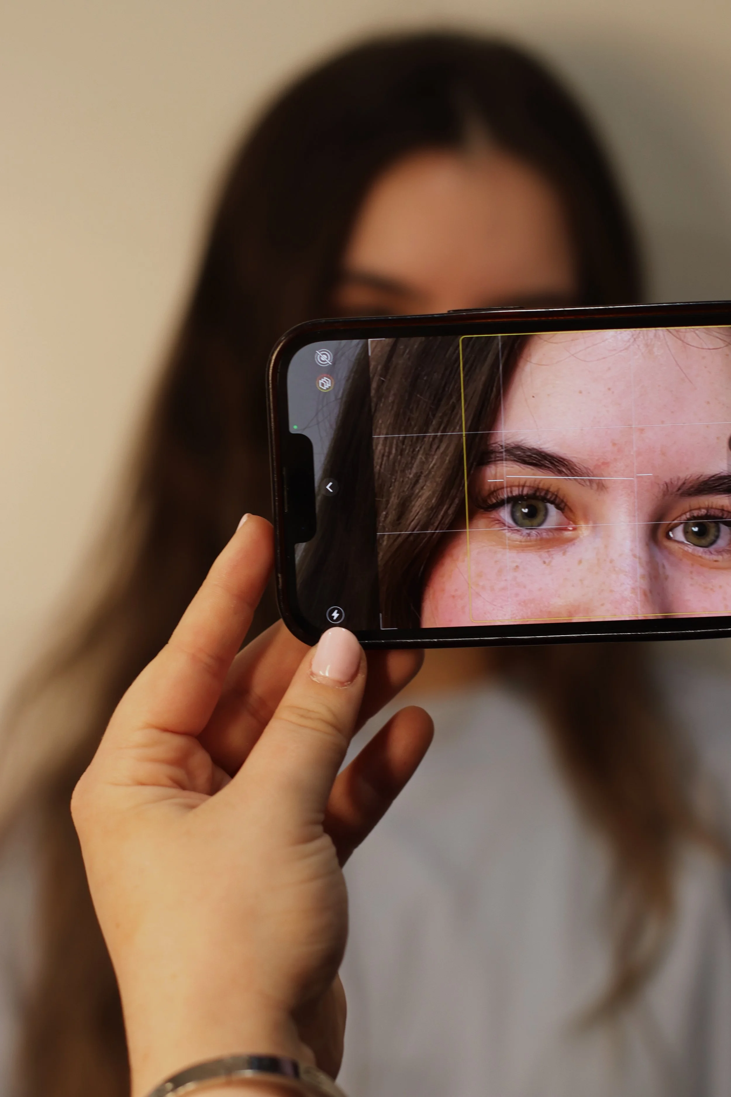 A person holding a smartphone in front of a woman's face, capturing an up-close photo of her eyes and upper face.