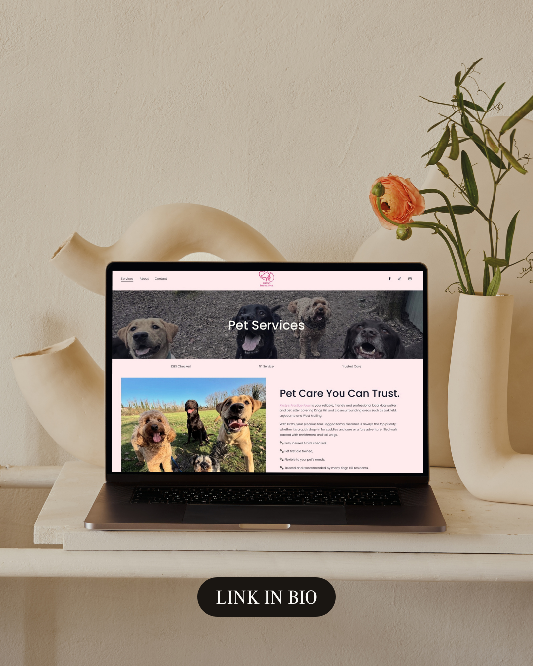 Laptop displaying a pet services website on a white shelf with a white vase and colorful flowers beside it.