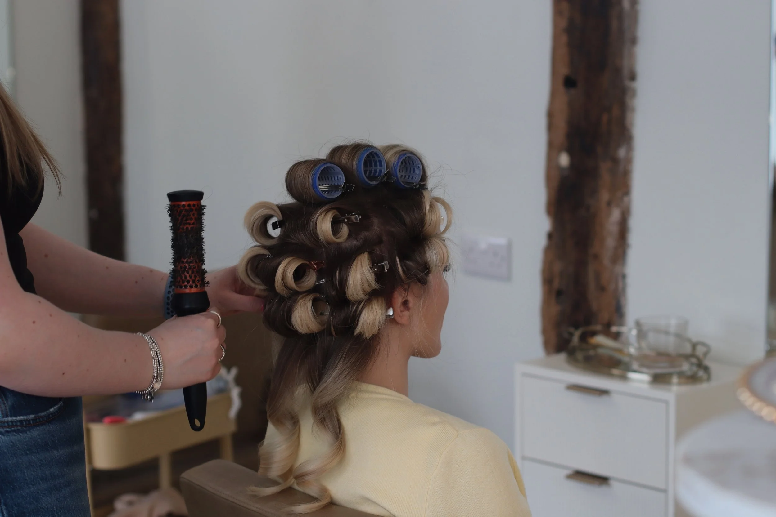 Woman getting her hair curled with rollers and a heated curling brush in a salon.