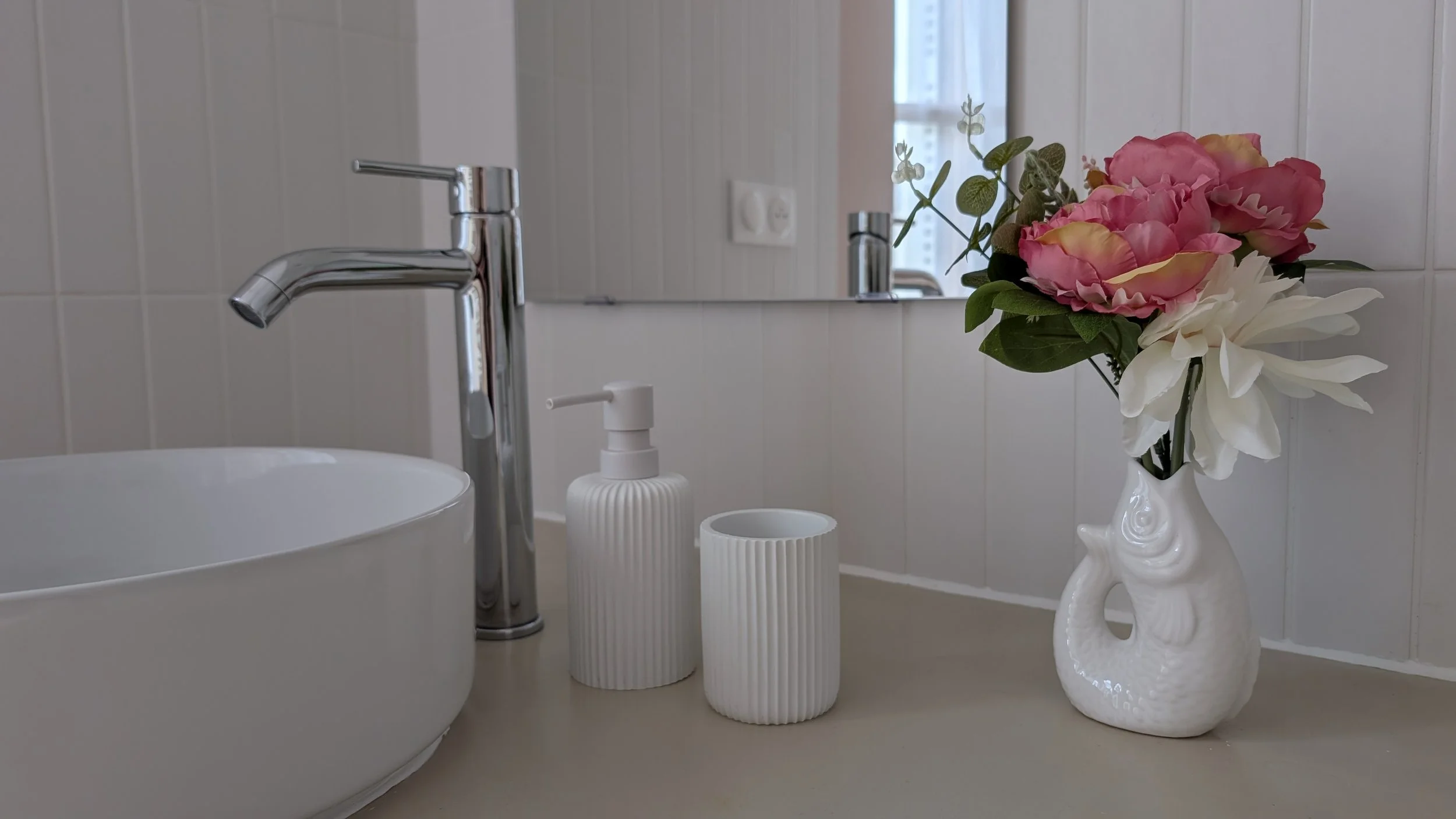Round sink, chrome faucet, soap dispensers, fish-shaped vase with flowers