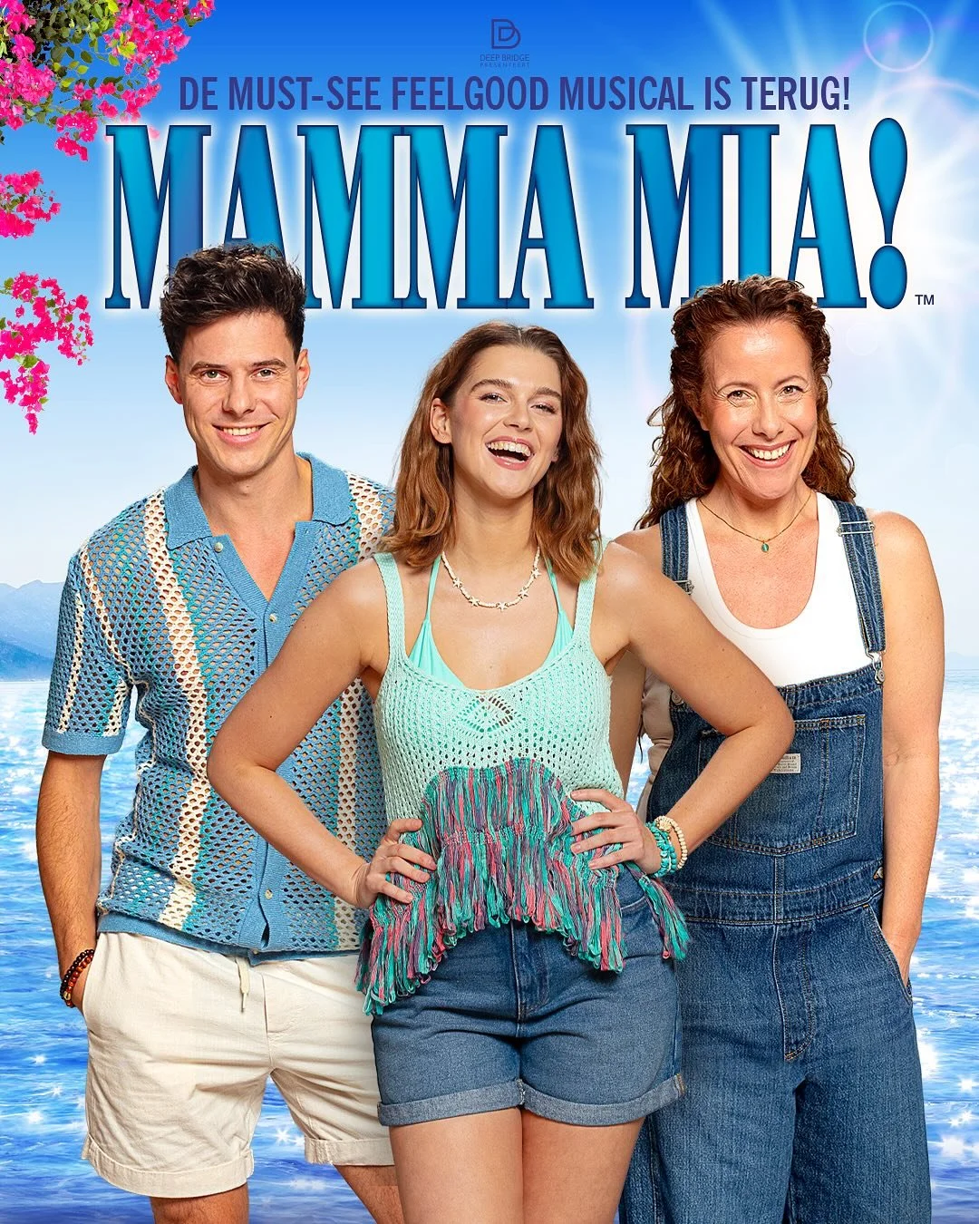 Promotiefoto van de musical Mamma Mia! met drie lachende acteurs voor een oceaanachtergrond en een blauwe lucht.