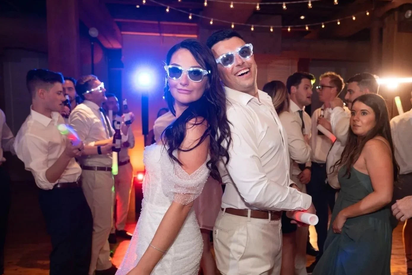 Bride and groom earring lighted sunglasses, dancing with wedding guests