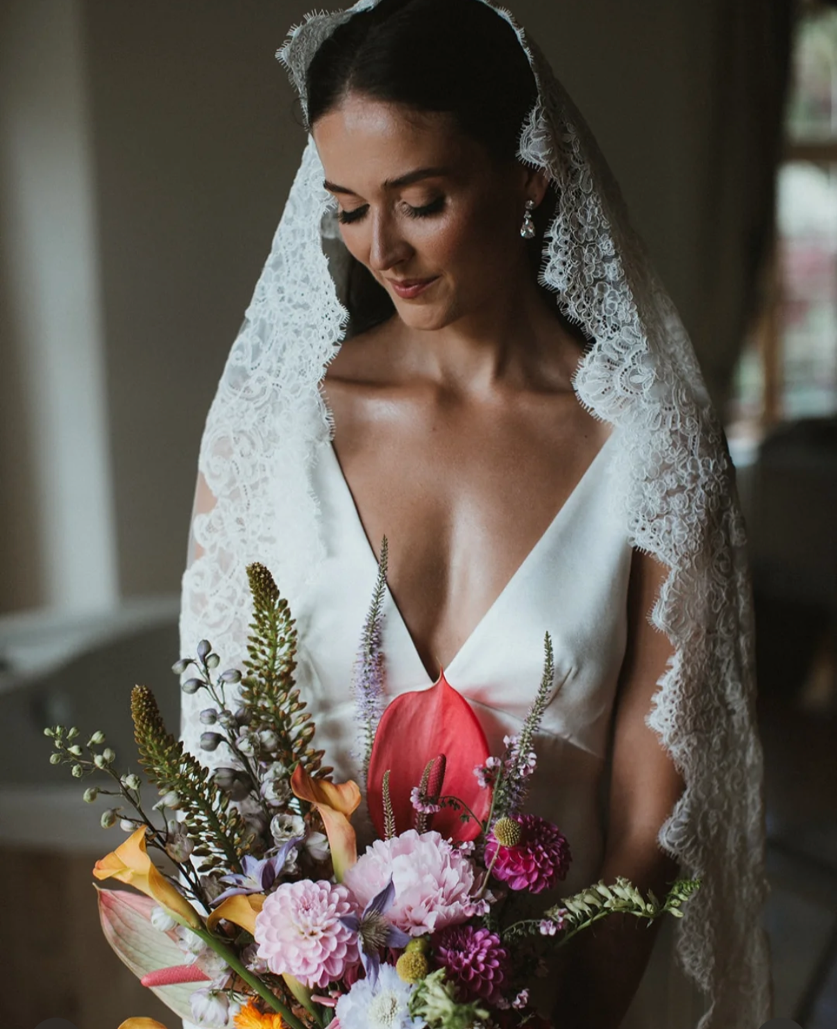 A bride in a satin dress with a lace veil holding a colorful bouquet of flowers