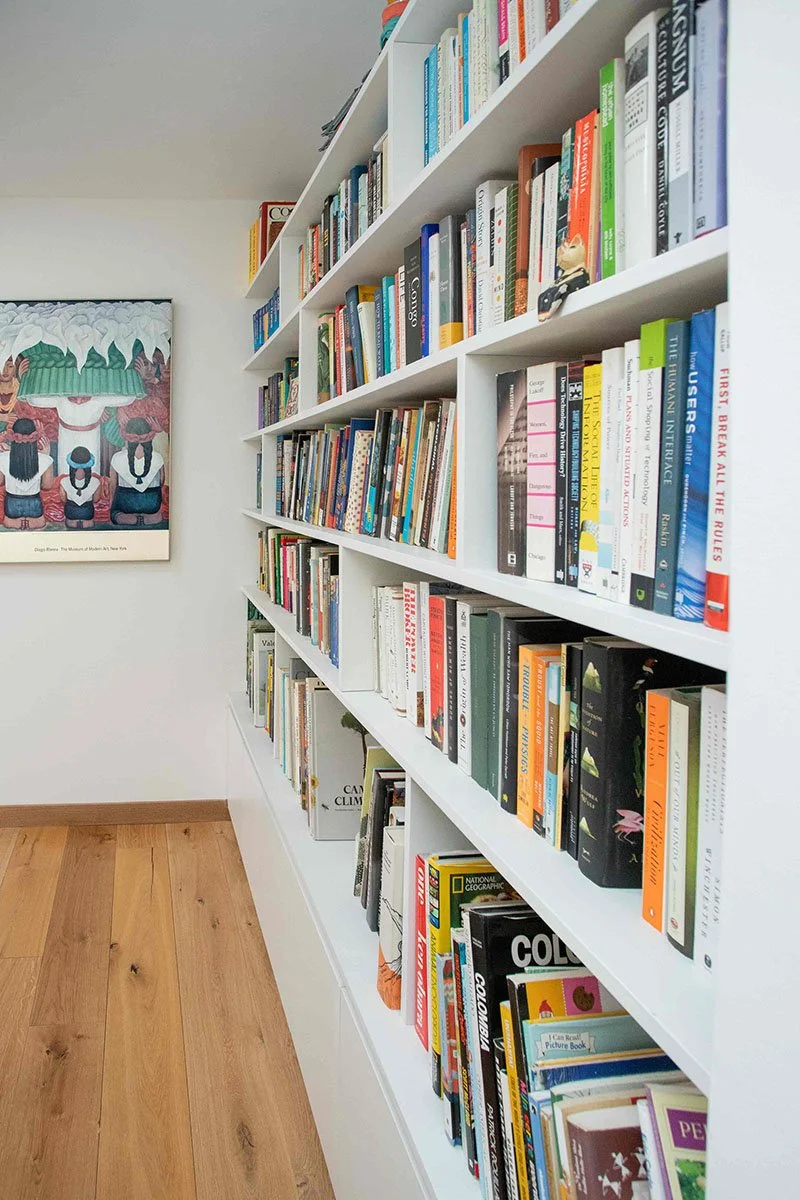 Estantería blanca con múltiples libros de diferentes colores y tamaños en una pared dentro de una casa.