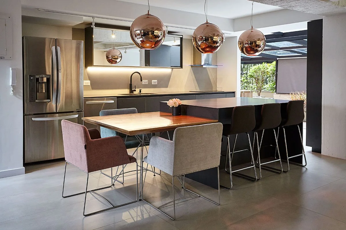 Cocina moderna con mesa de comedor, sillas de colores, frigorífico y lámparas de techo cromadas.
