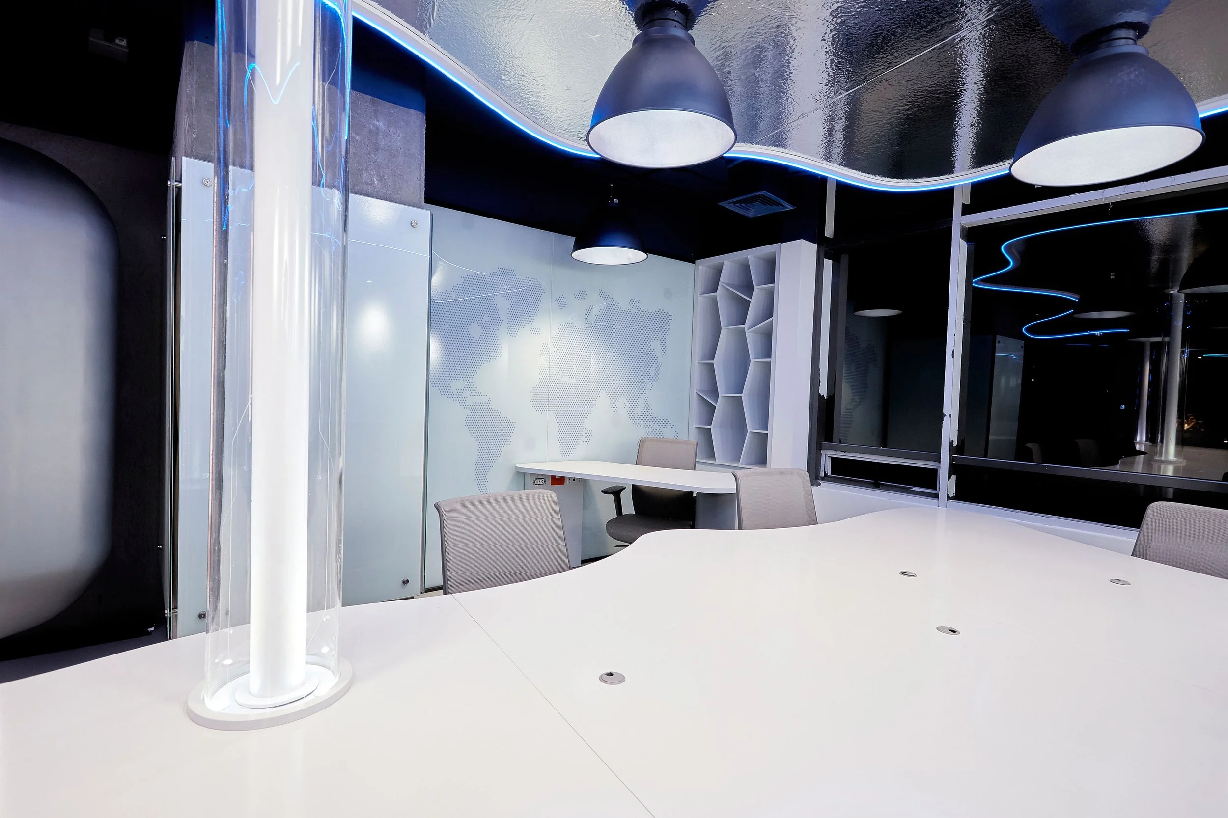 Sala de reuniones moderna con paredes blancas, mobiliario gris y luces LED azules en el techo.