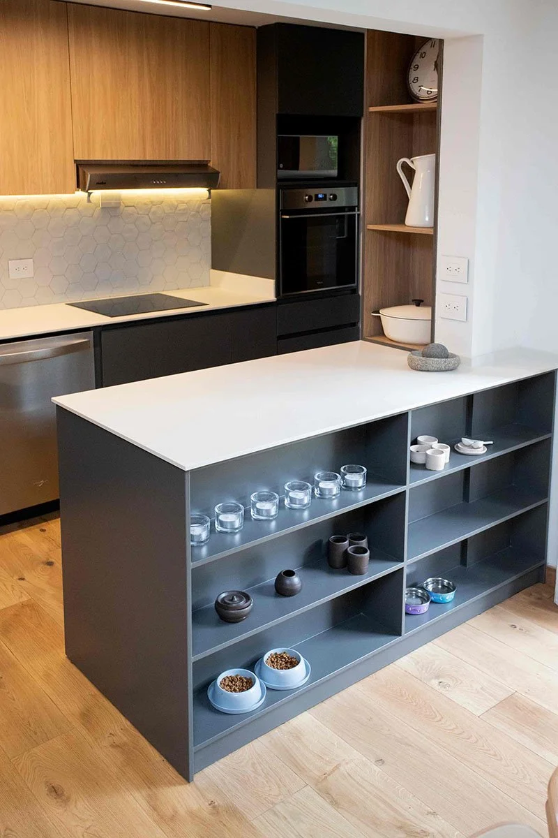 Cocina moderna con estantería gris con platos y tazones, encimera blanca, electrodomésticos integrados, paredes con azulejos hexagonales y decoración minimalista.