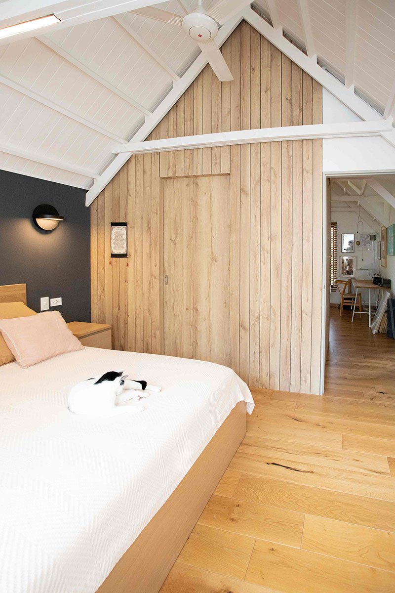 Habitación moderna con cama de madera, pared de madera, lámpara de pared negra, ventilador en el techo y un gato acostado sobre la cama.