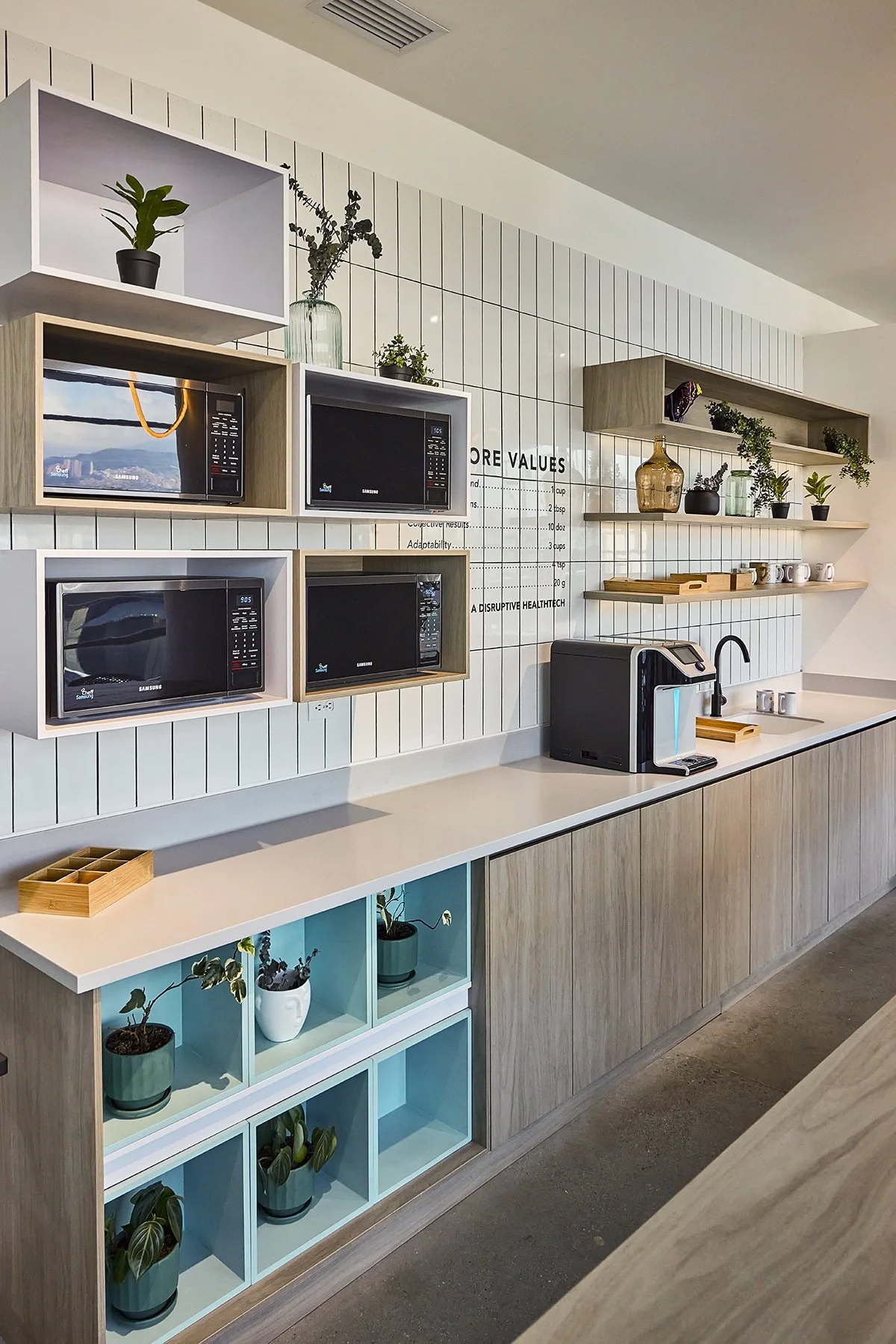 Oficina moderna con estantes decorativos, microondas, máquina de agua y plantas en la pared y en la repisa.
