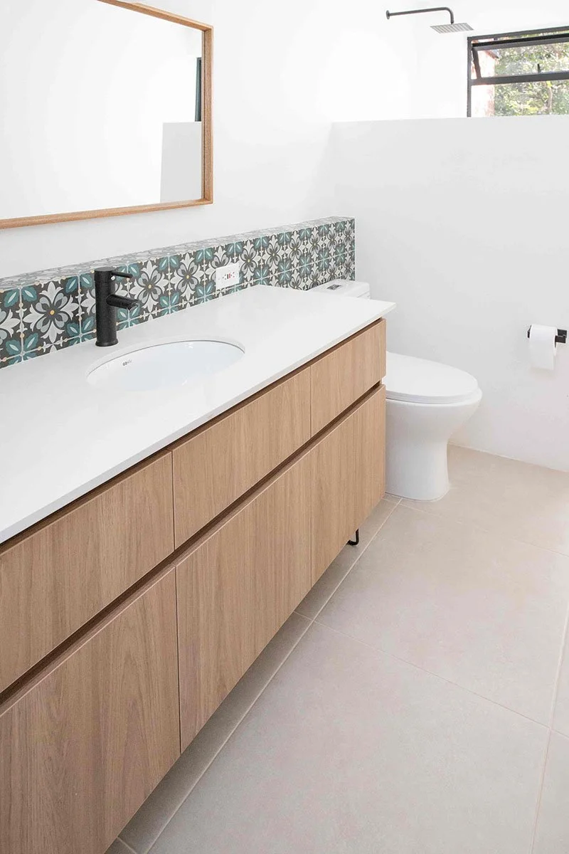 Lavabo con mueble de madera, espejo, inodoro, papel higiénico y ducha con ventana en baño moderno.