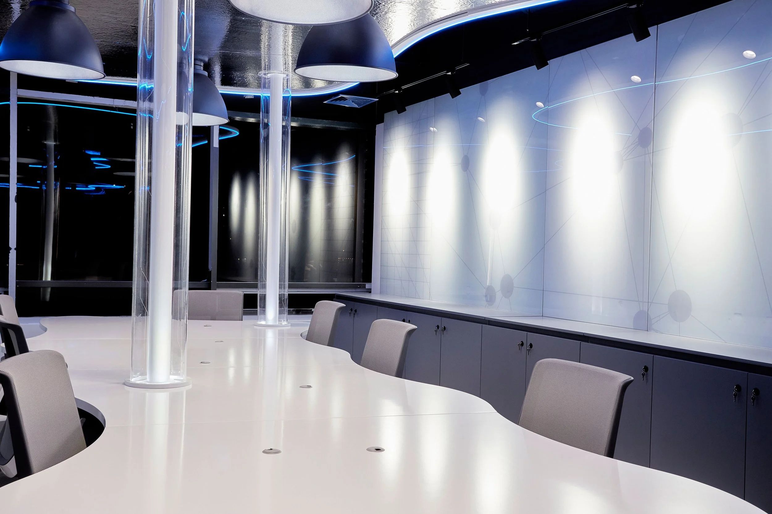 sala de conferencias moderna con mesa blanca, sillas grises, paredes blancas con gráficos y luces LED azules.