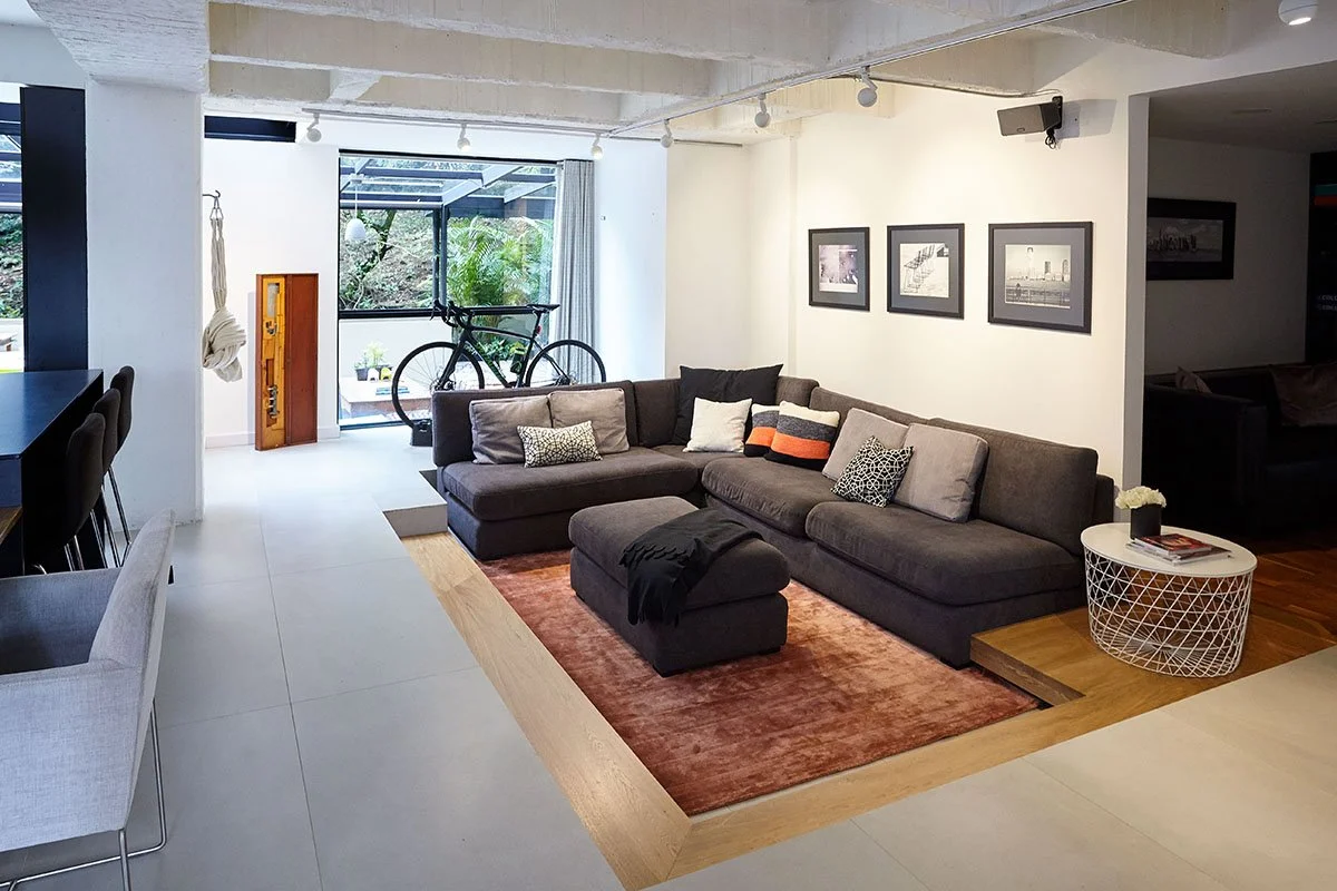 Sala de estar moderna con sofá gris, mesa de centro blanca, cuadros en la pared, bicicleta junto a la ventana y decoración minimalista.