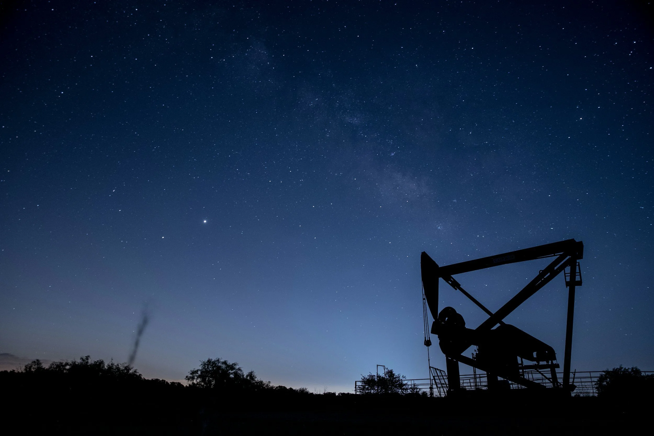 Silhouette of an oil pumpjack against a starry night sky with the Milky Way visible.