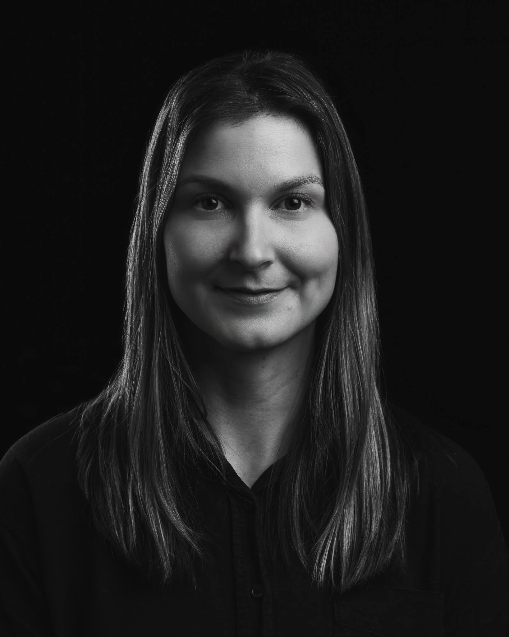 Mustavalkoinen kuva nuoresta naisesta, jolla pitkät hiukset ja hymy, taustana musta väri.