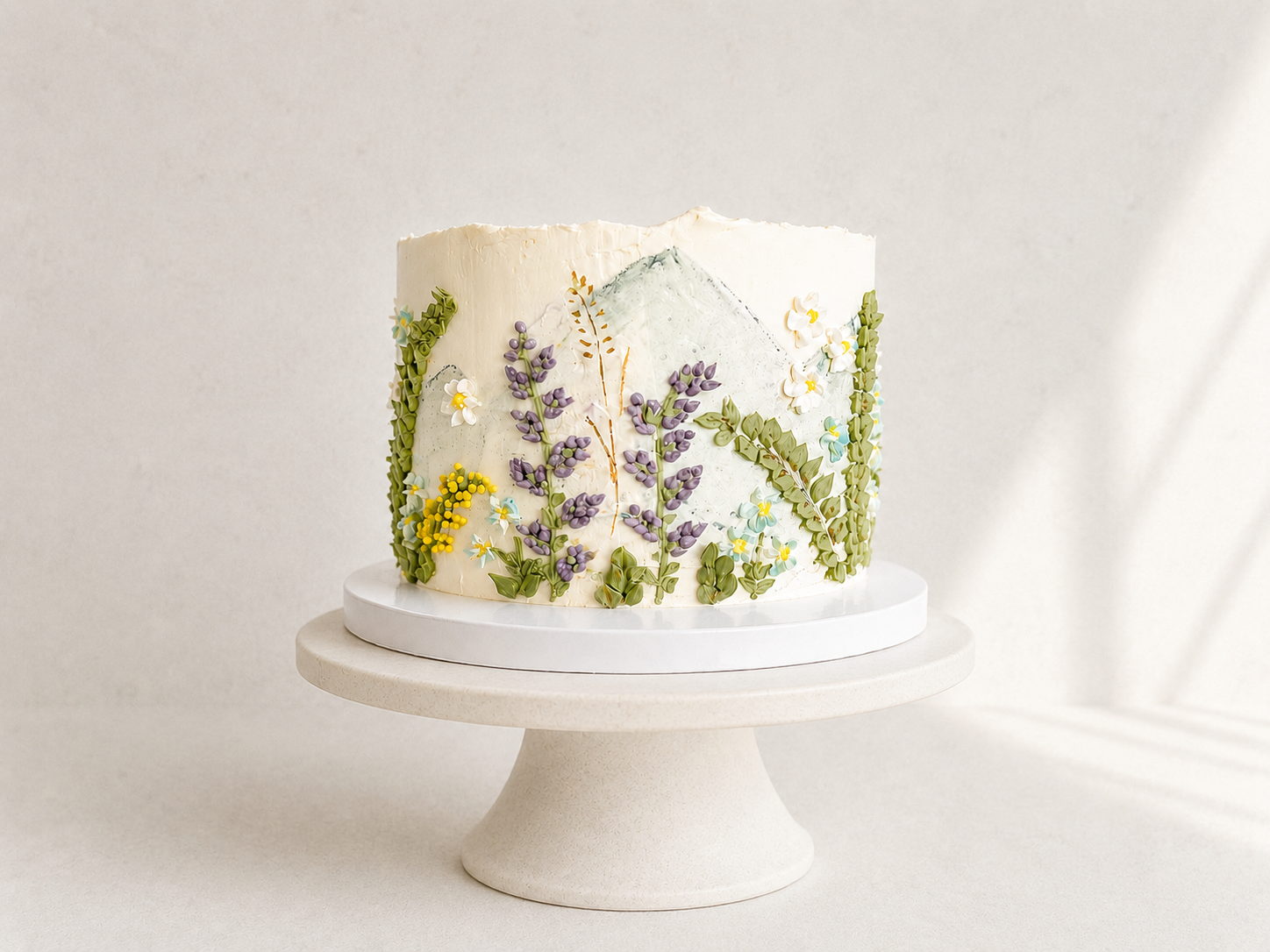 Mountain-inspired celebration cake decorated with hand-piped wildflowers and buttercream details, handcrafted in Dublin by Full Bloom Bakehouse. This all-buttercream cake features dark chocolate sponge, coffee ganache and blackcurrant mousse for a ri