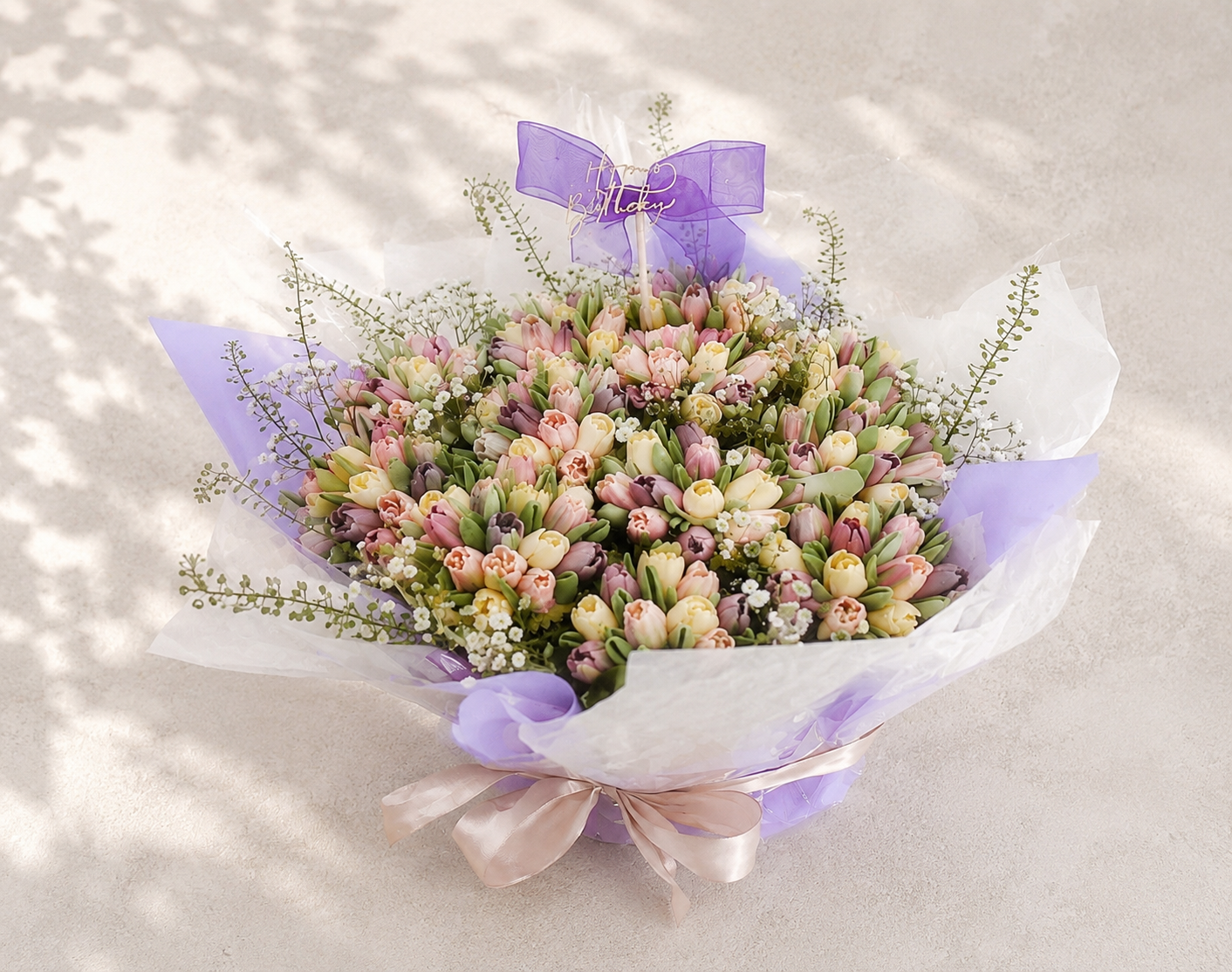 Hand-piped pastel tulip cupcake bouquet with real greenery, beautifully wrapped in lilac paper and handcrafted in Dublin by Full Bloom Bakehouse. A luxury floral cupcake bouquet and elegant alternative to fresh flowers, perfect for birthdays, Mother’