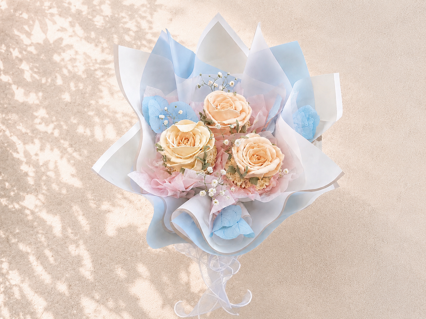 Three-cupcake bouquet featuring hand-piped blush and peach roses, beautifully wrapped in soft blue and pink paper, handcrafted in Dublin by Full Bloom Bakehouse. A luxury cupcake bouquet and elegant edible gift, perfect for birthdays, baby showers, M