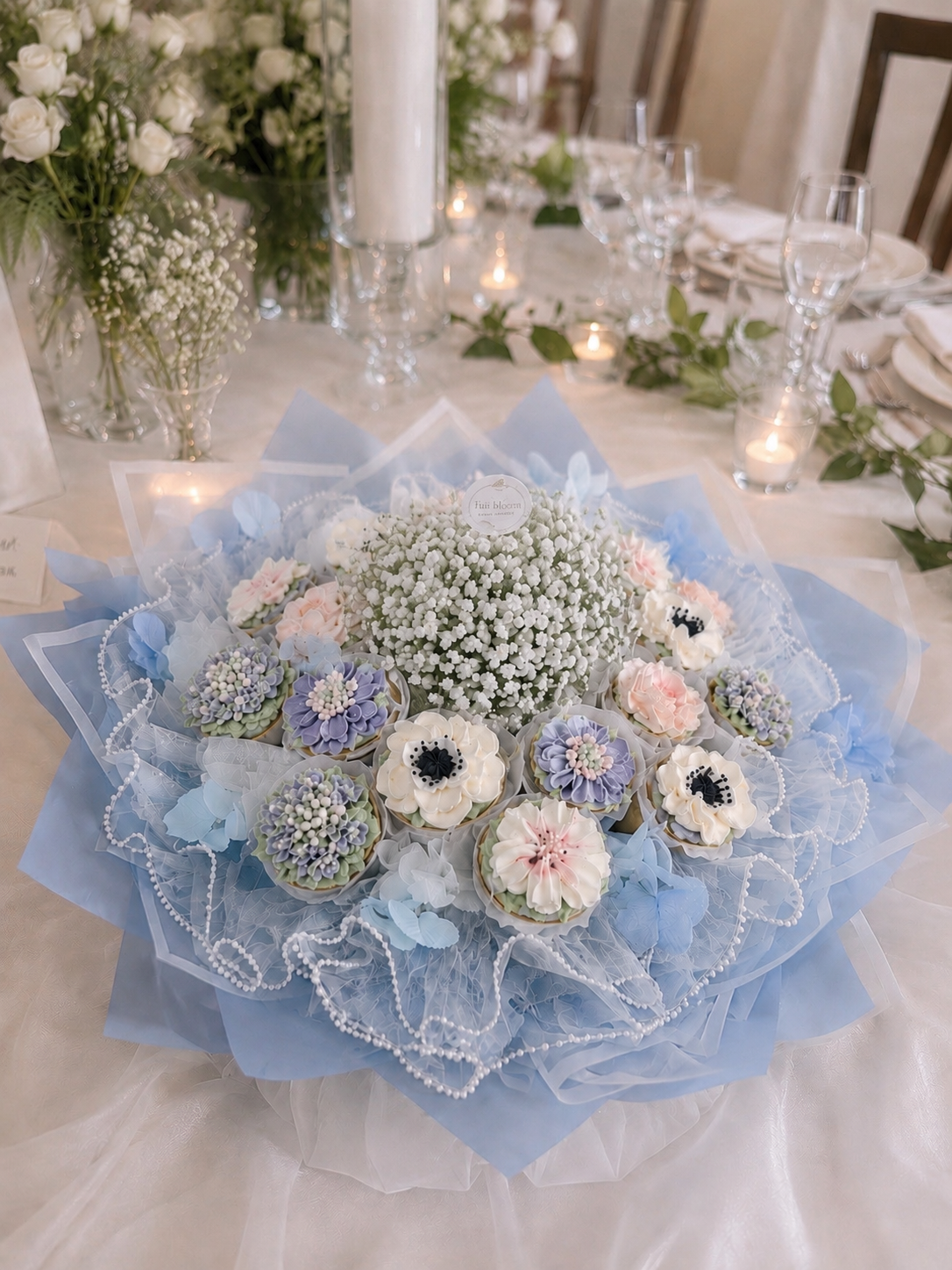 Wedding cupcake bouquet featuring soft blue and blush pink buttercream flowers, delicate blue eucalyptus details and gypsophila centrepieces, beautifully wrapped in white and light blue paper. Handcrafted in Dublin by Full Bloom Bakehouse and filled 