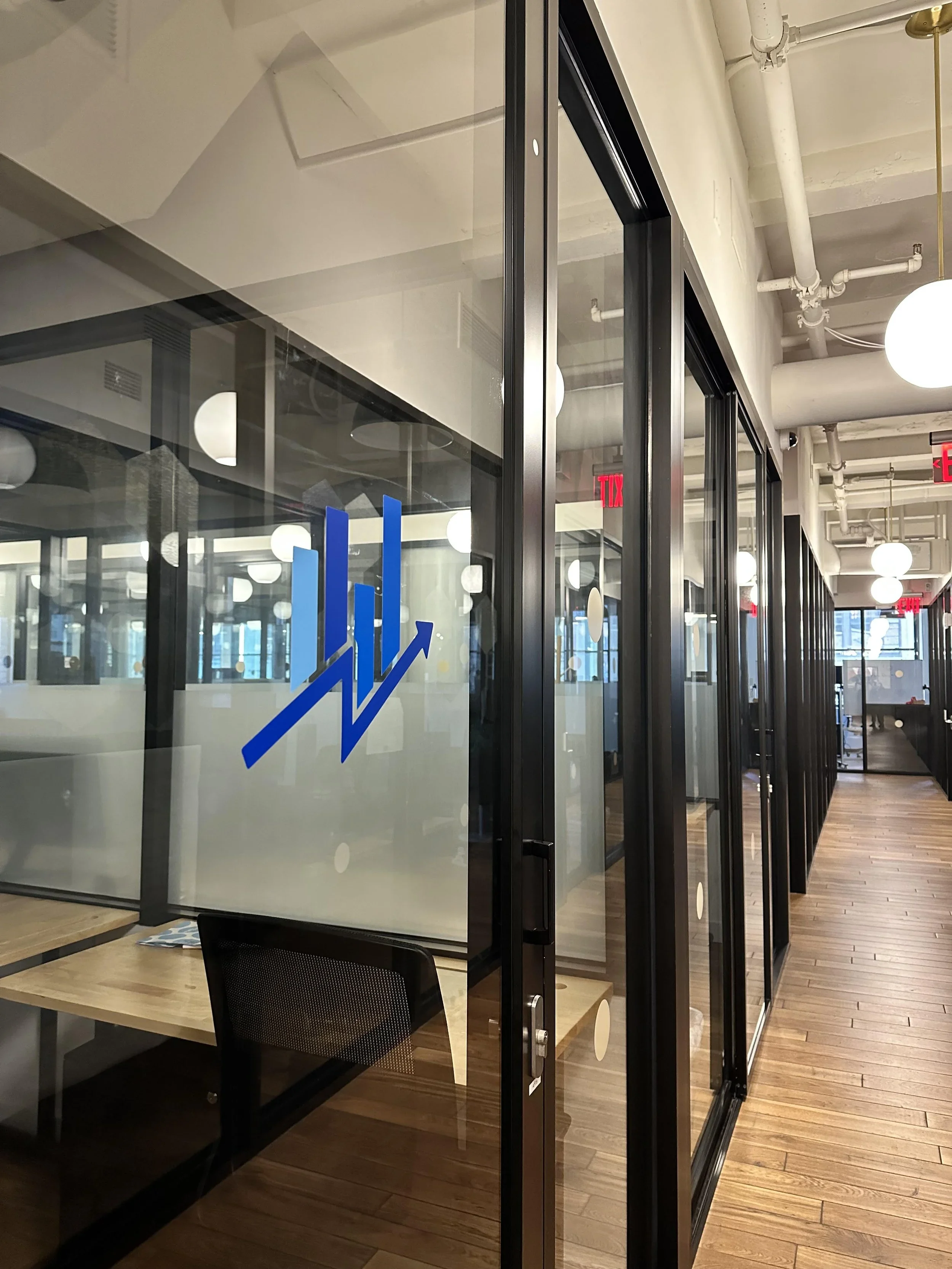 Modern office interior with glass partitions, wooden flooring, and round white ceiling lights.
