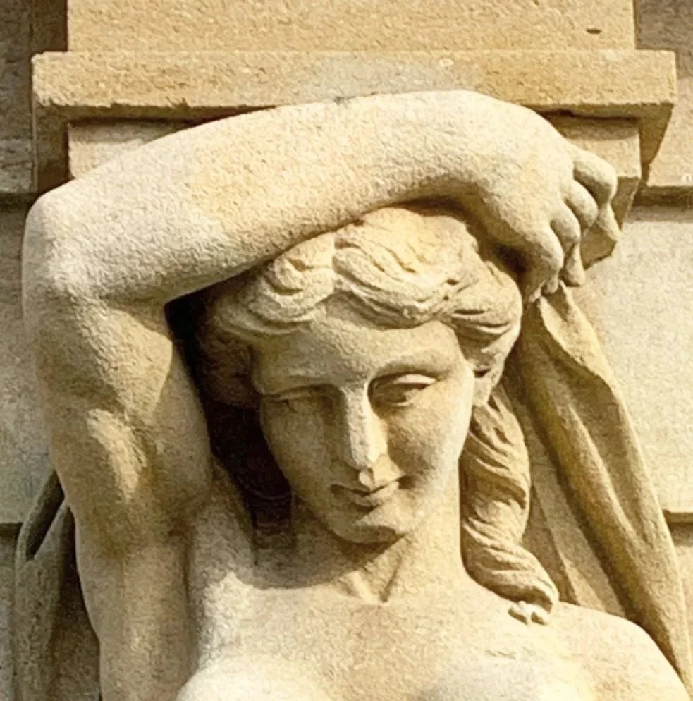Close-up view of a carved stone sculpture of a woman with her hand resting on her forehead, exhibiting a serene expression.