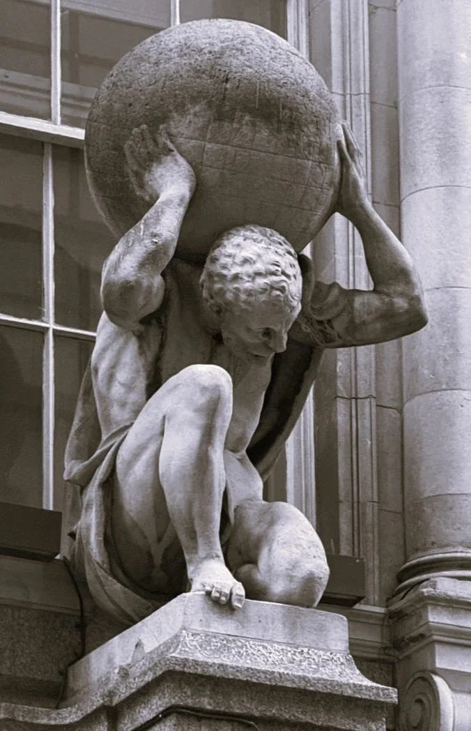 A marble statue of a muscular man holding a large globe on his shoulders, crouching on a pedestal.