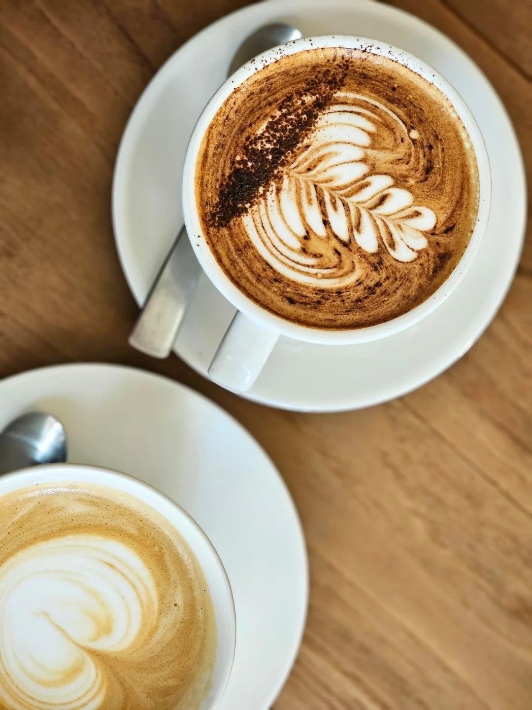 Two cups of coffee with latte art on a wooden table.