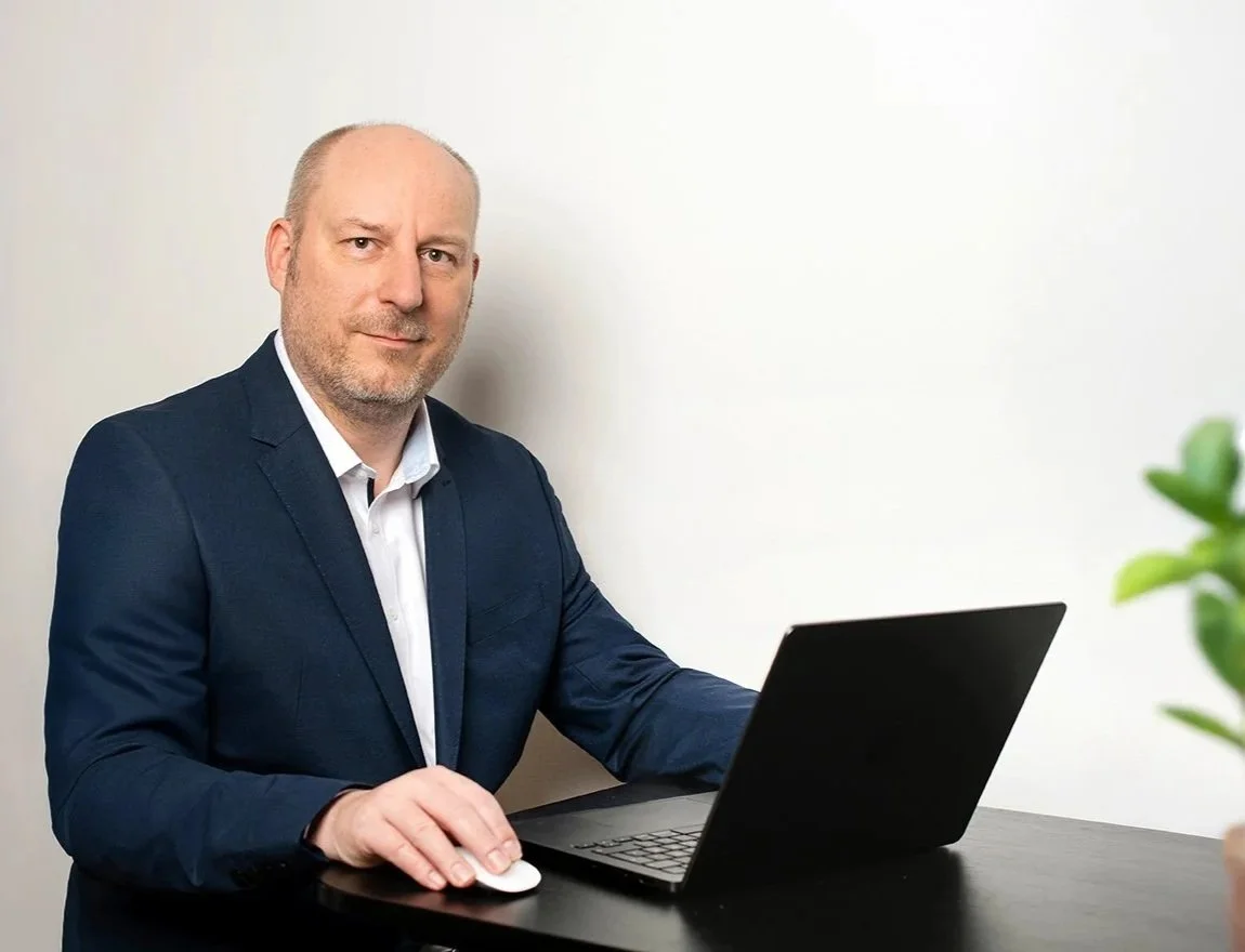 Dr. med. Sebastian Kramer im dunklen Anzug sitzt an einem schwarzen Tisch vor einem Laptop und erstellt eine radiologische Zweitmeinung.