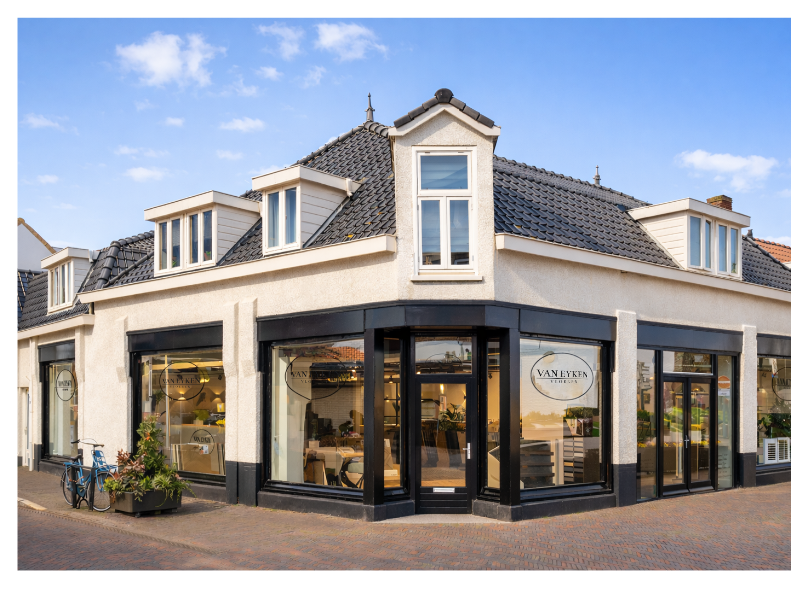 Corner view of a two-story building with a flower shop on the ground floor and residential windows on the upper floor, under a blue sky with scattered clouds.