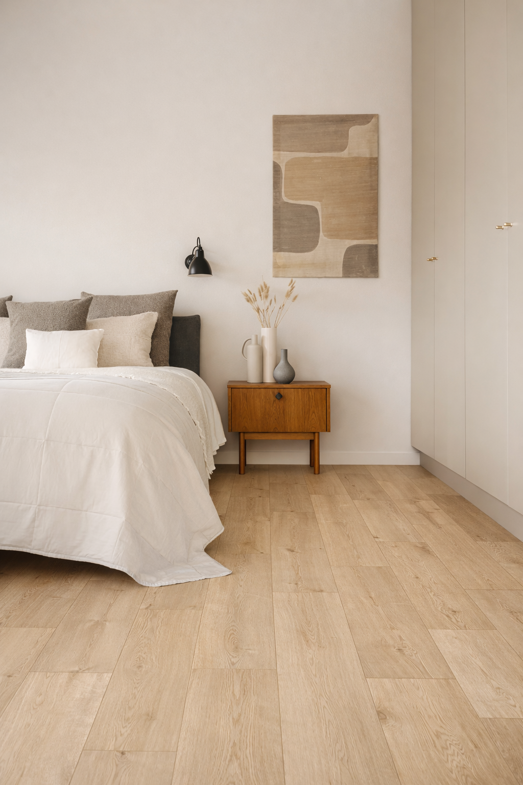 A minimalist bedroom with a bed, a nightstand with decorative vases, a wall-mounted lamp, and abstract wall art.
