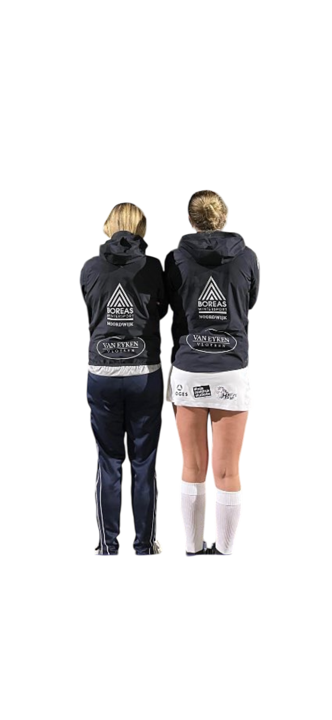 Two female athletes in sports uniforms standing with their backs facing the camera, wearing black Nissan jackets. The athlete on the right is in a white tennis skirt and knee-high socks, while the one on the left is in dark athletic pants.
