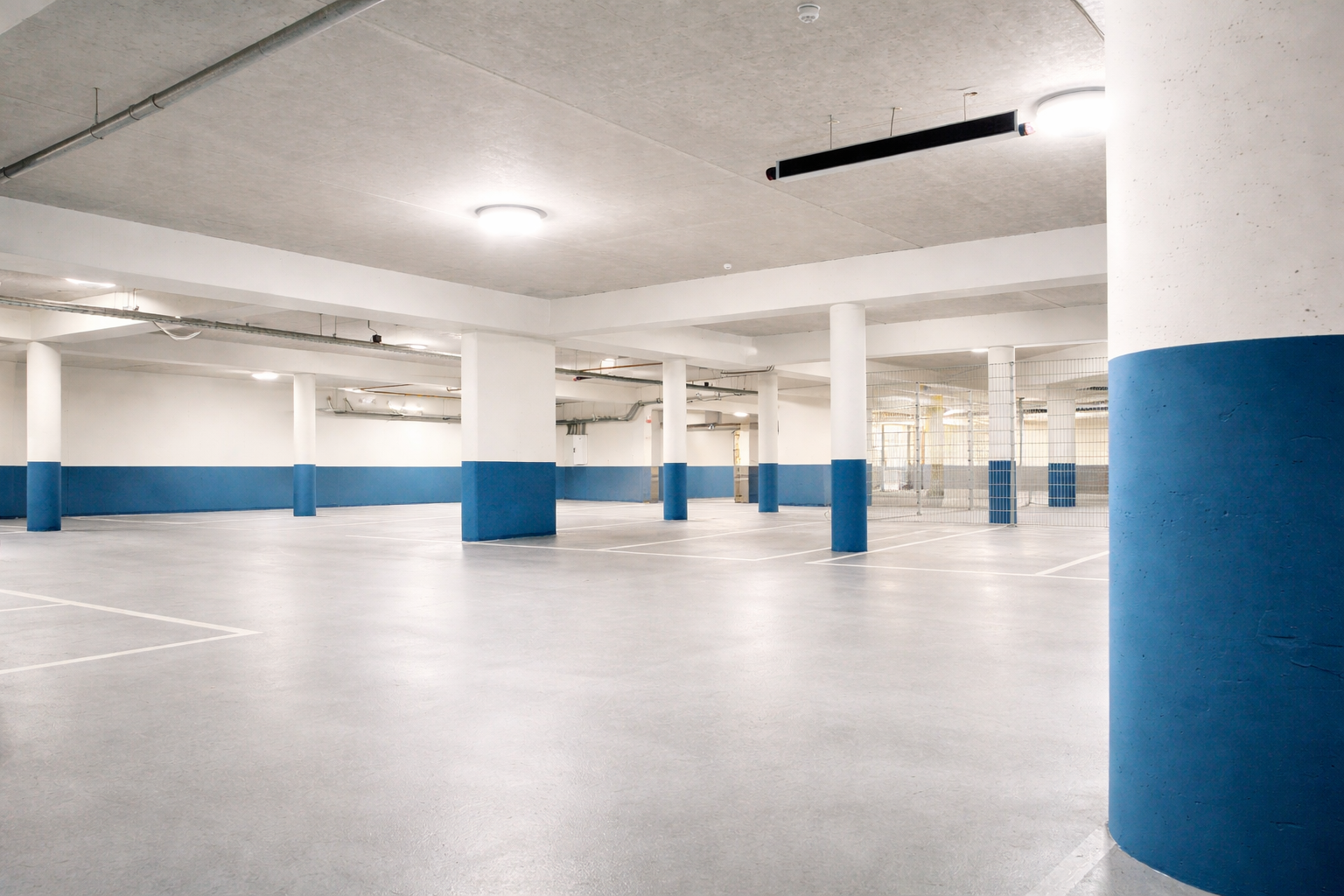 Empty underground parking garage with white and blue painted columns, fluorescent lights, and a concrete ceiling.
